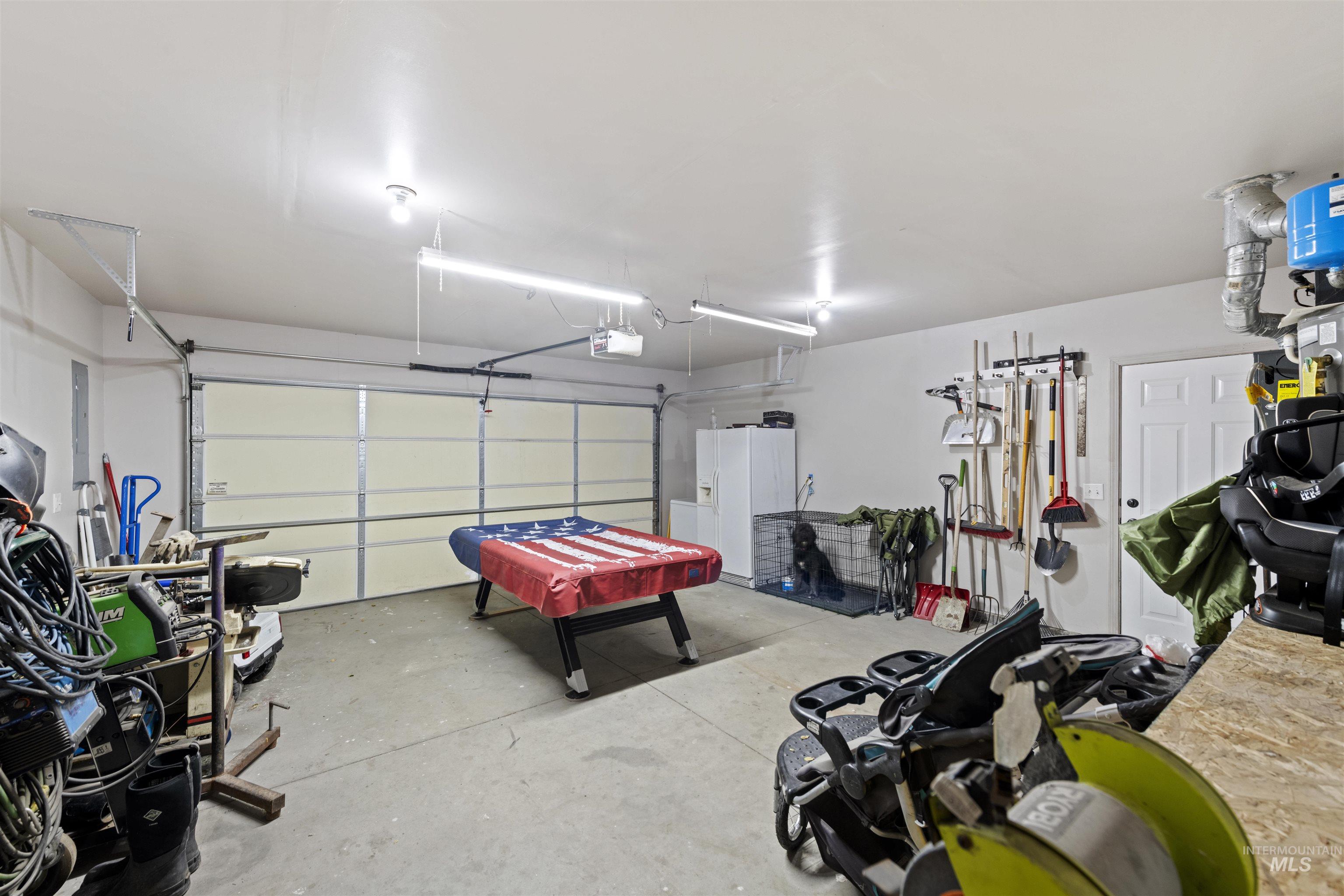 Garage with white fridge with ice dispenser, electric panel, and a garage door opener