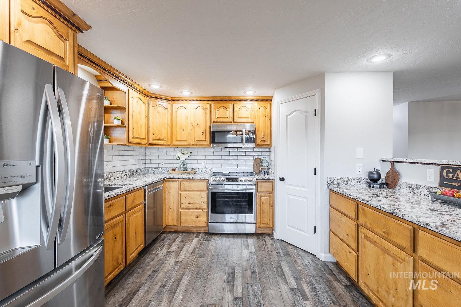 Kitchen featuring stainless steel appliances, light stone counters, decorative backsplash, open shelves, and recessed lighting