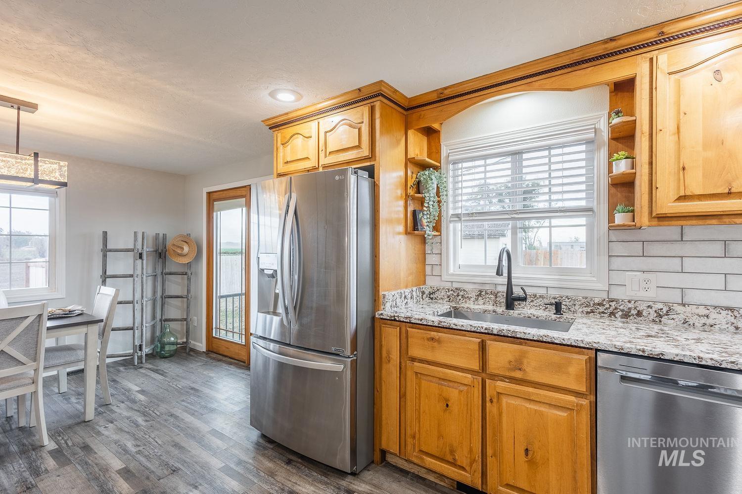 Kitchen with appliances with stainless steel finishes, healthy amount of natural light, light stone countertops, and dark wood-style flooring