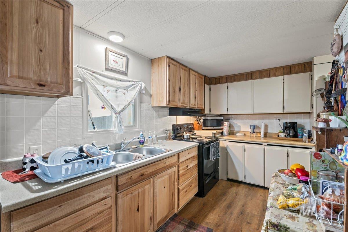 Kitchen featuring black electric range oven, light countertops, dark wood-type flooring, decorative backsplash, and a textured ceiling