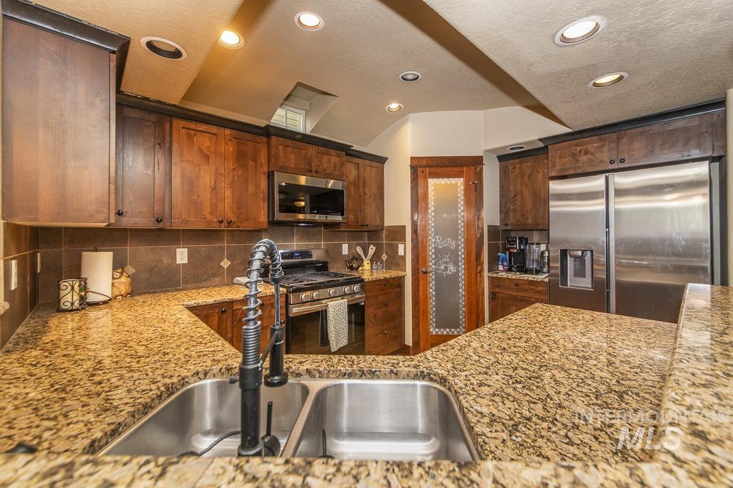 Kitchen with appliances with stainless steel finishes, light stone countertops, recessed lighting, tasteful backsplash, and a textured ceiling