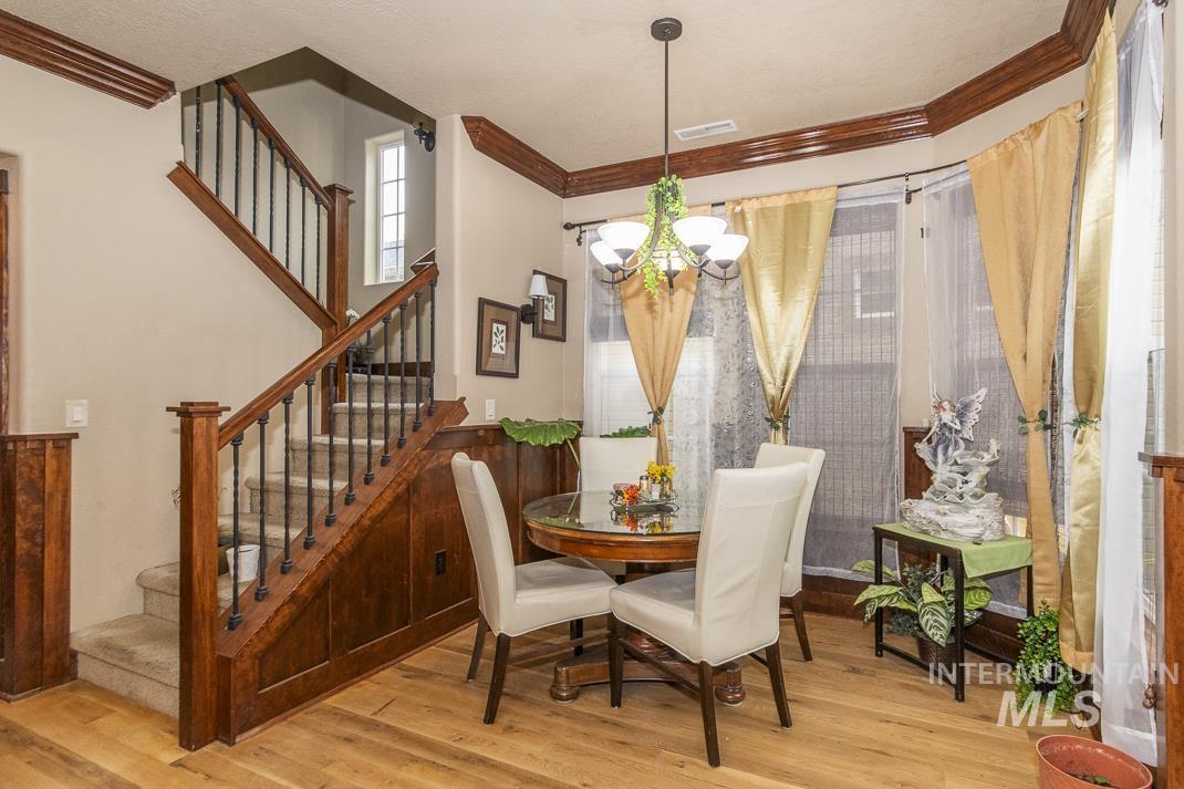 Dining space with crown molding, light wood finished floors, a chandelier, and stairs