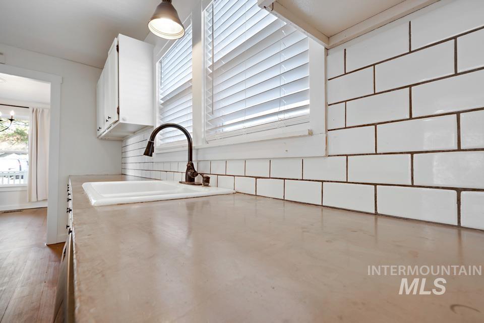 Kitchen with white cabinetry, light countertops, tasteful backsplash, a chandelier, and hanging light fixtures
