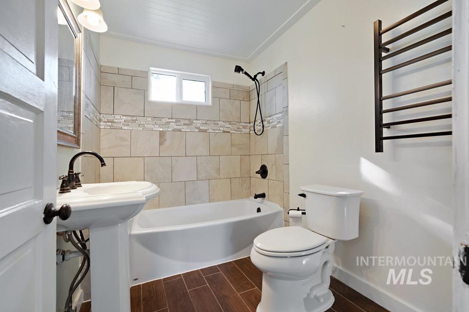 Bathroom with wood tiled floors, shower / bath combination, radiator, and a towel warming rack