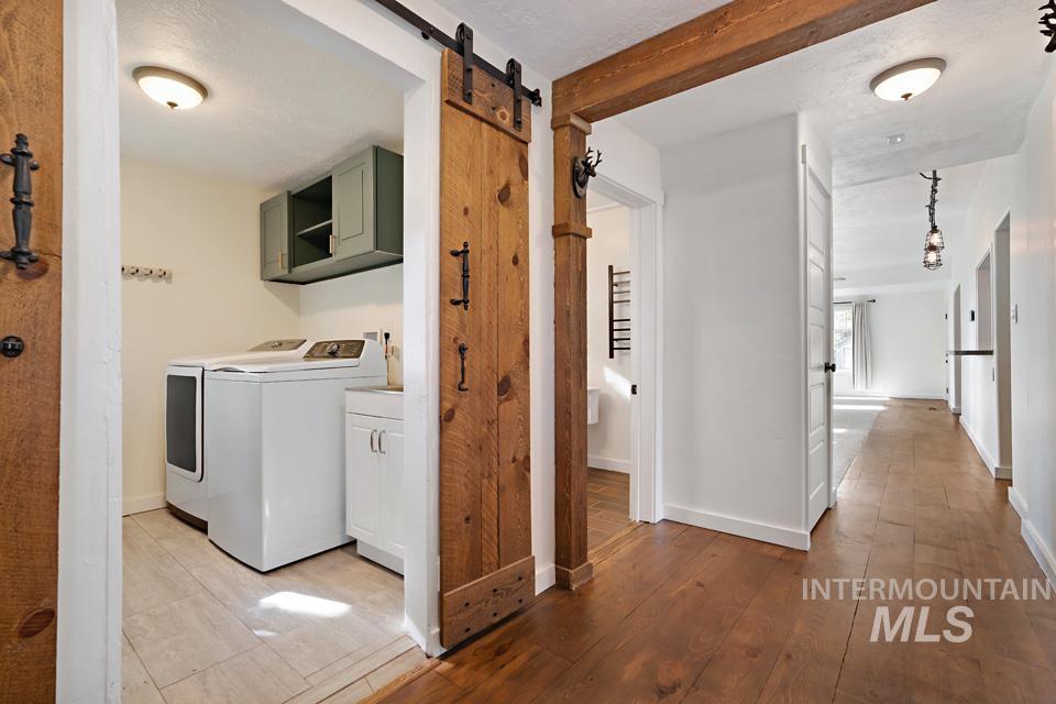 Laundry room featuring cabinet space, a barn door, light wood-style floors, washing machine and clothes dryer, and beam ceiling