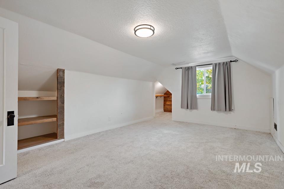 Additional living space with lofted ceiling, light colored carpet, and a textured ceiling
