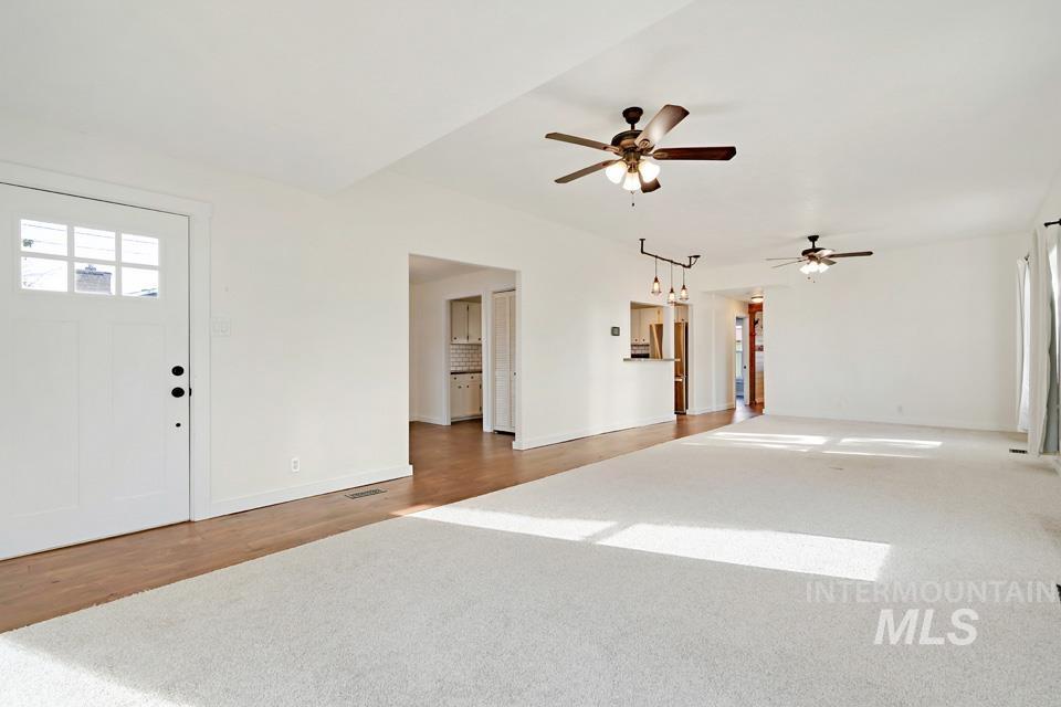 Unfurnished living room with light wood-style flooring, light colored carpet, and ceiling fan