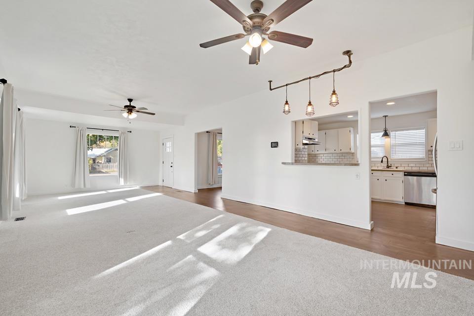 Unfurnished living room with healthy amount of natural light, ceiling fan, dark carpet, and dark wood-style floors