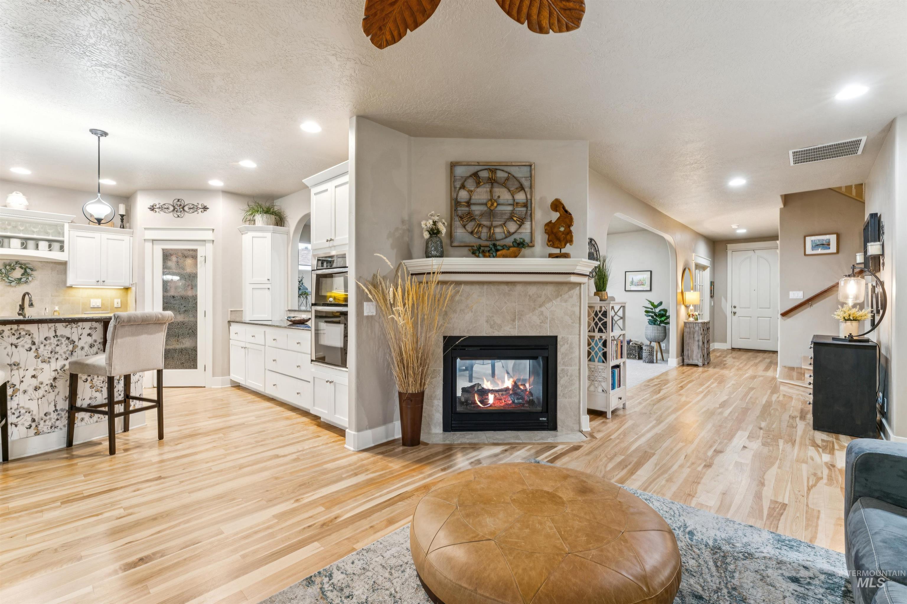 Living area featuring light wood finished floors, a multi sided fireplace, recessed lighting, arched walkways, and a textured ceiling