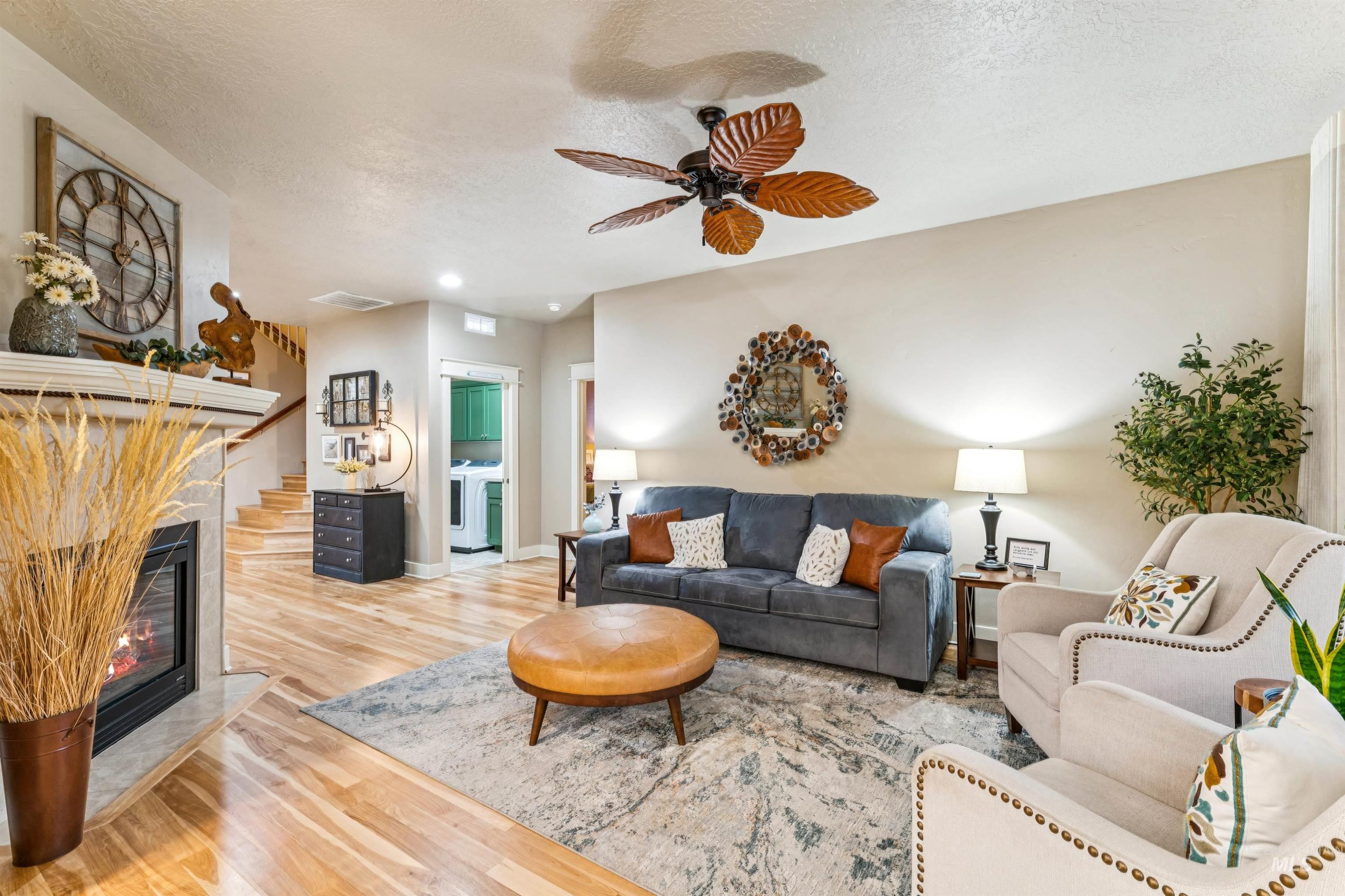 Living room featuring wood finished floors, a textured ceiling, a glass covered fireplace, a ceiling fan, and stairway