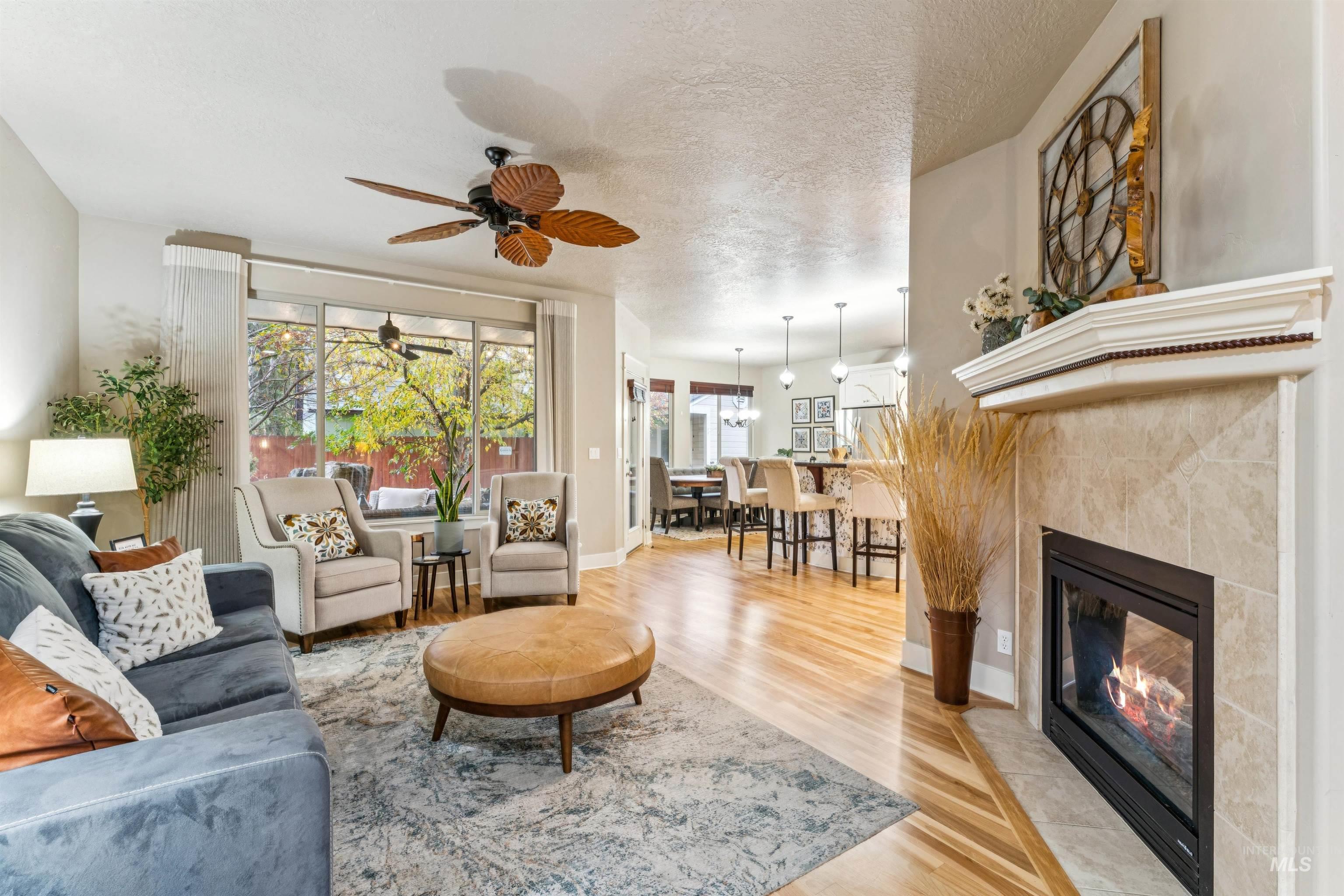 Living area featuring light wood-style floors, a fireplace, ceiling fan, and a textured ceiling