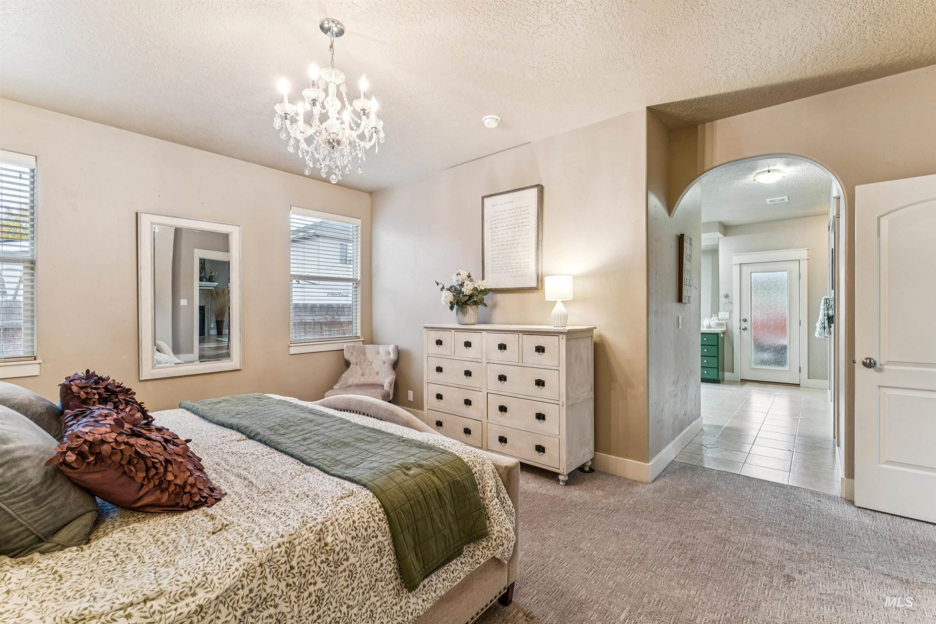 Carpeted bedroom with arched walkways, a textured ceiling, tile patterned floors, and a chandelier