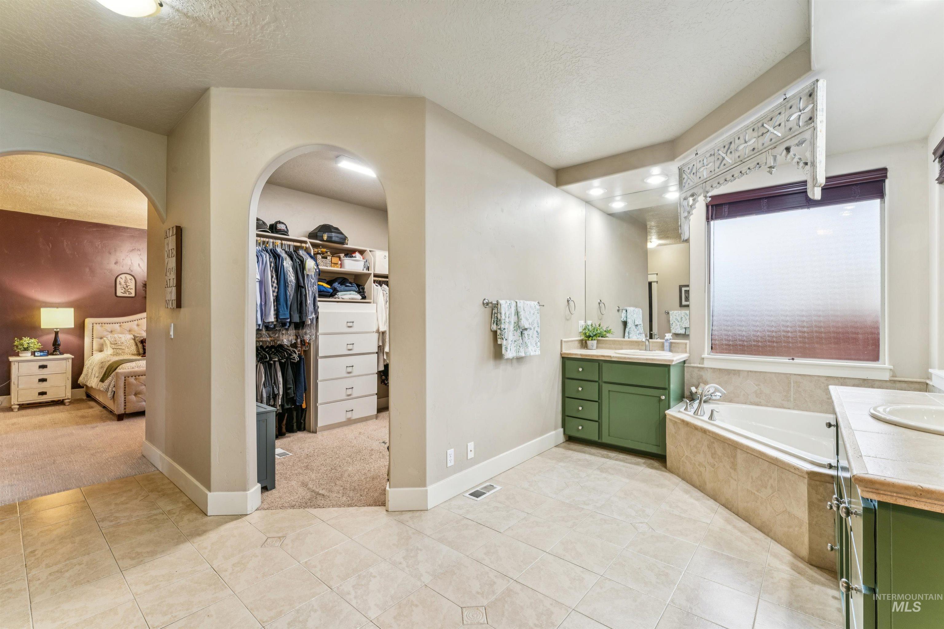 Bathroom with vanity, a bath, light tile patterned floors, a textured ceiling, and a walk in closet