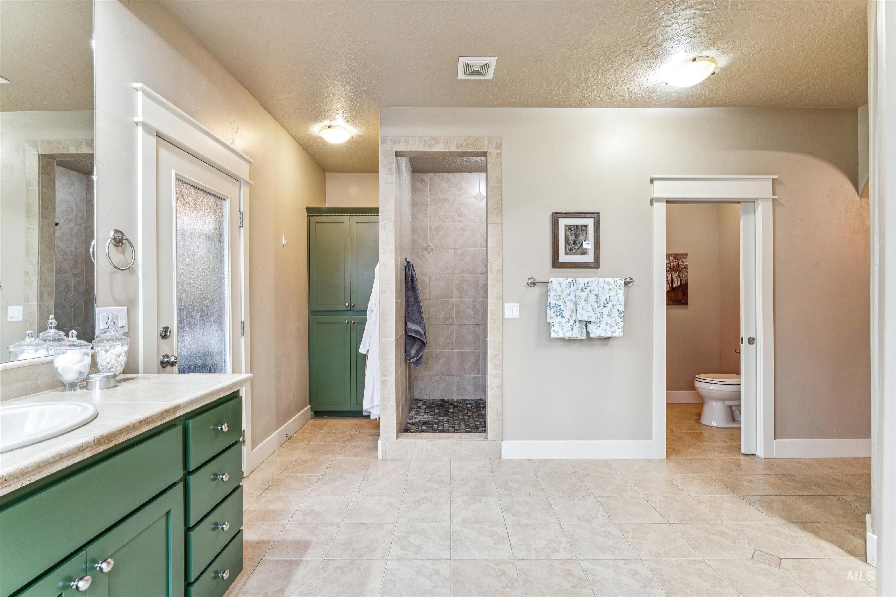 Bathroom featuring a textured ceiling, light tile patterned floors, tiled shower, and vanity