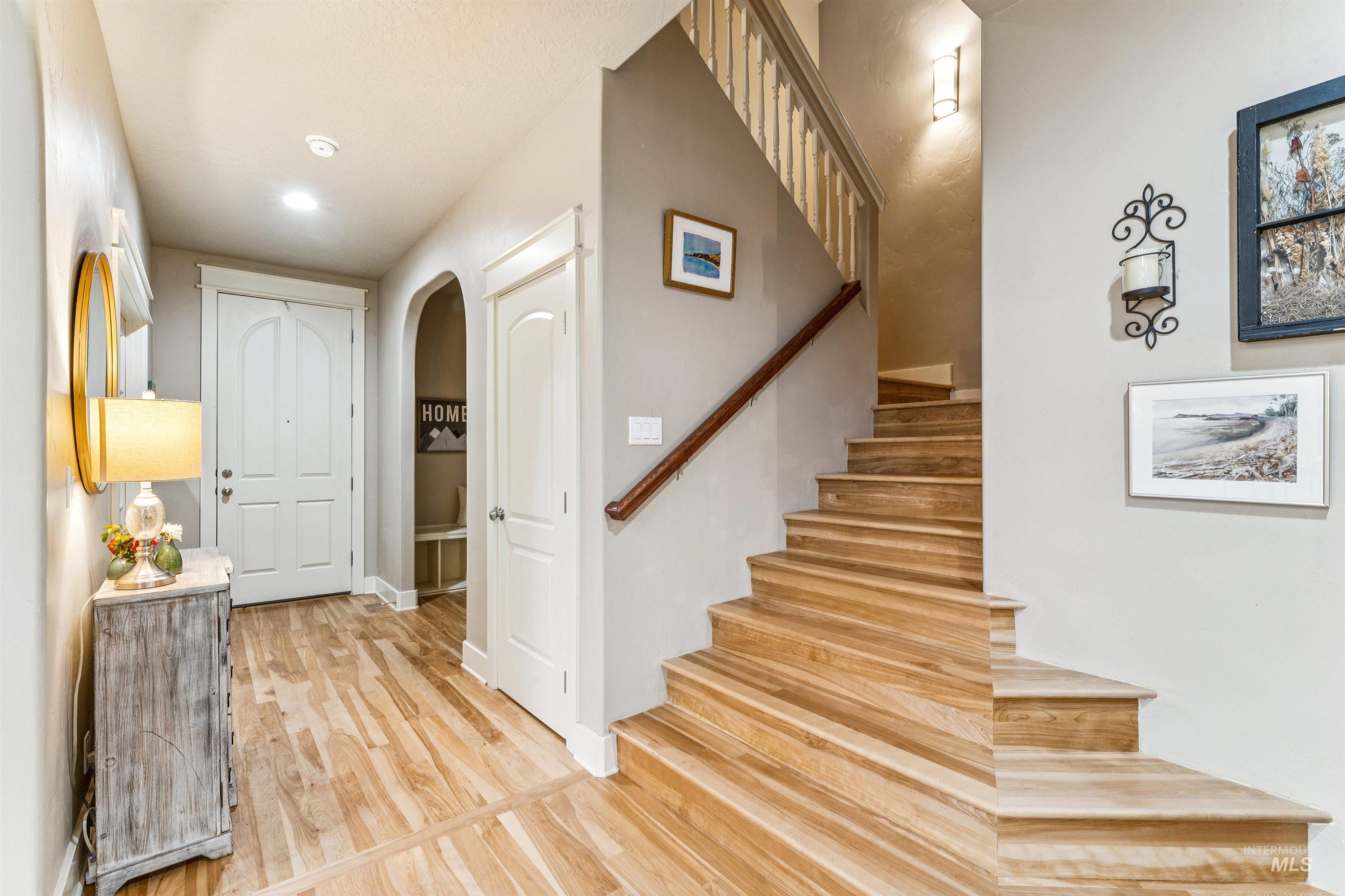 Foyer with arched walkways, light wood-style floors, stairs, and recessed lighting