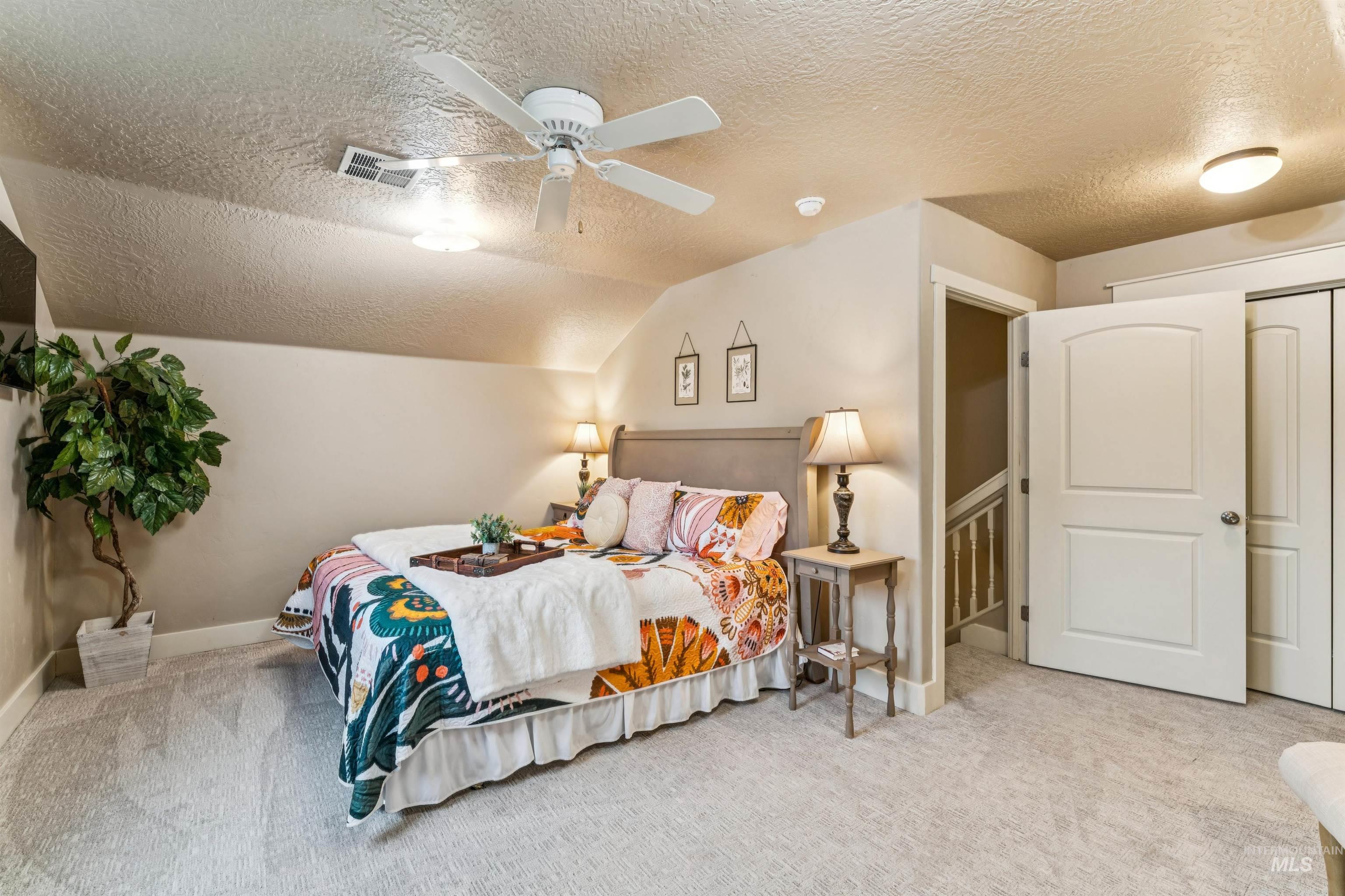 Bedroom with a textured ceiling, light colored carpet, ceiling fan, and vaulted ceiling