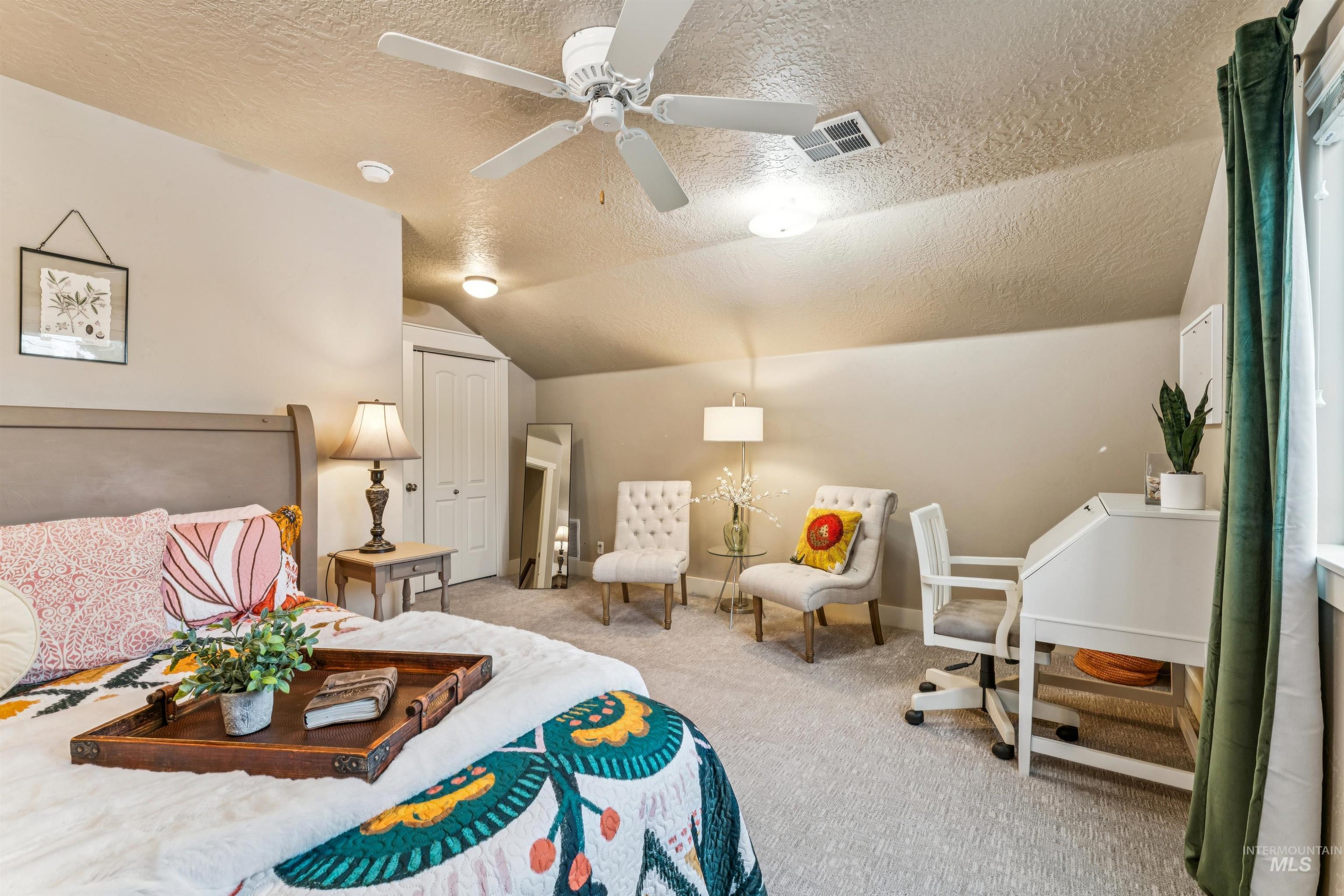 Carpeted bedroom featuring a textured ceiling, vaulted ceiling, and ceiling fan