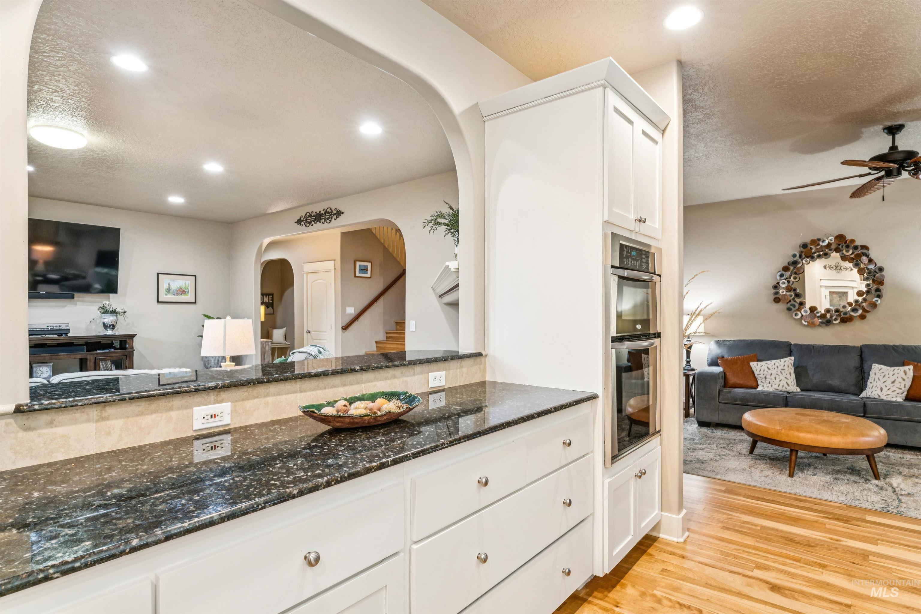 Kitchen featuring open floor plan, white cabinets, dark stone countertops, light wood-style floors, and a ceiling fan