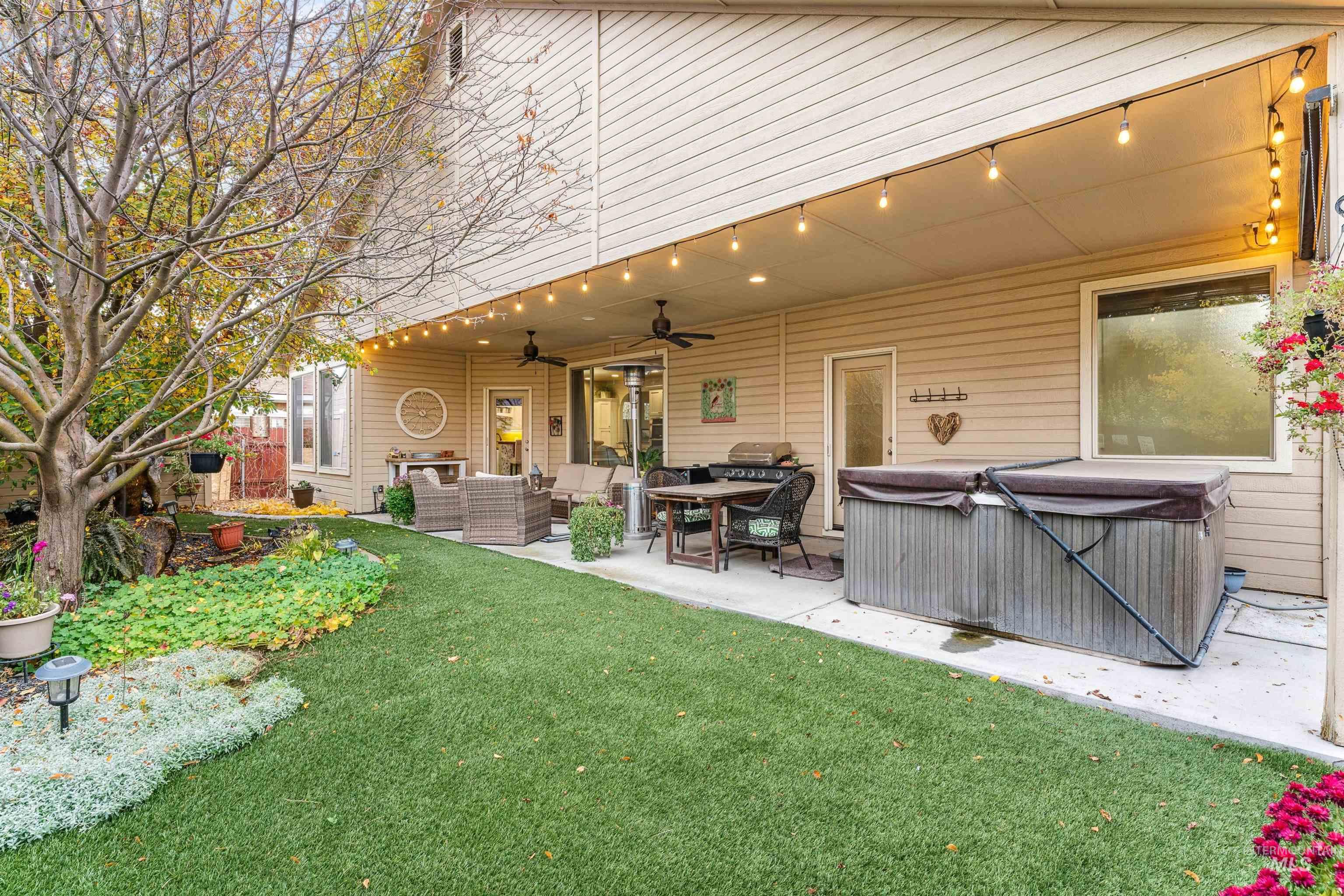 Back of property with a ceiling fan, outdoor lounge area, a patio area, a yard, and a hot tub