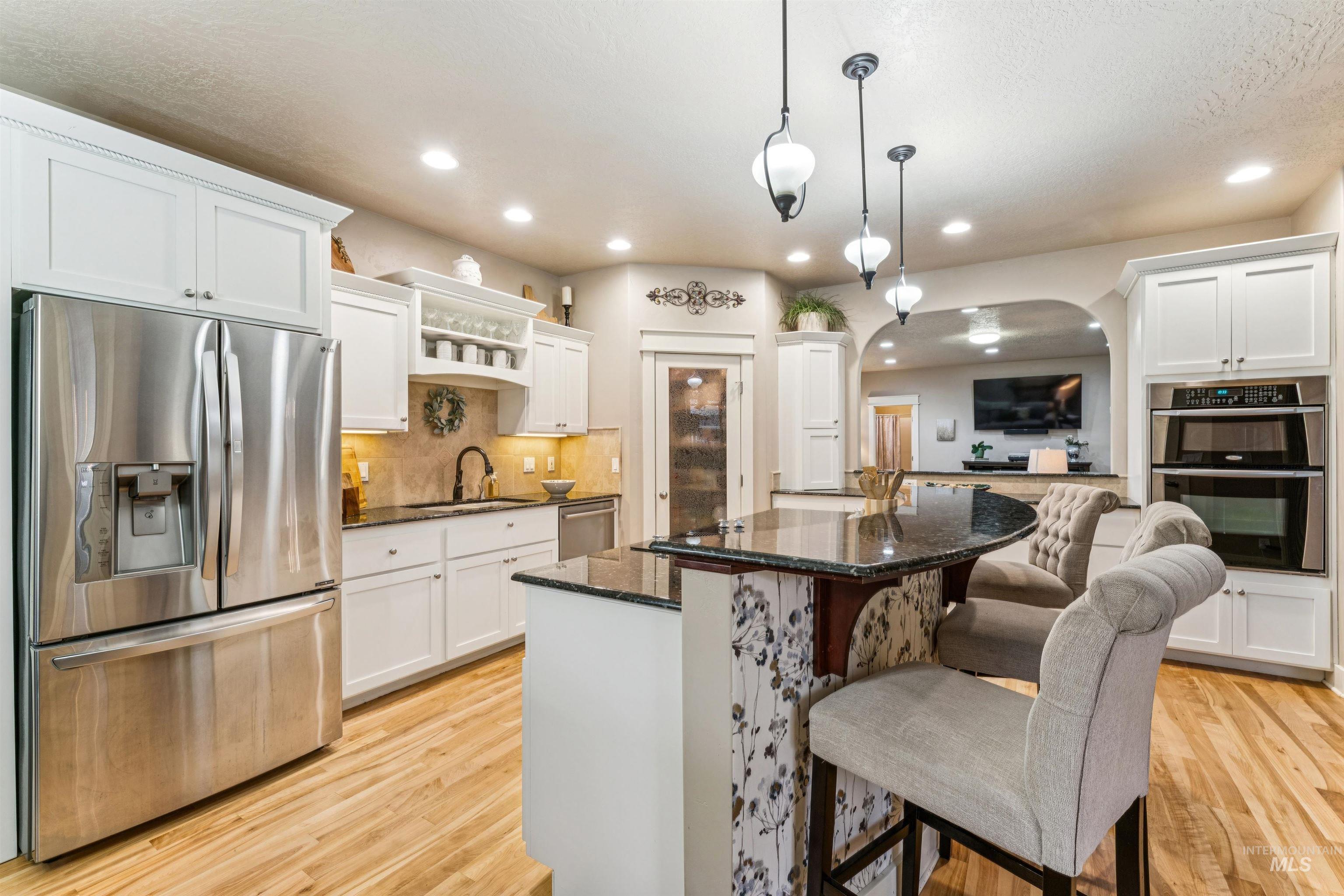Kitchen featuring appliances with stainless steel finishes, dark stone countertops, white cabinetry, arched walkways, and recessed lighting
