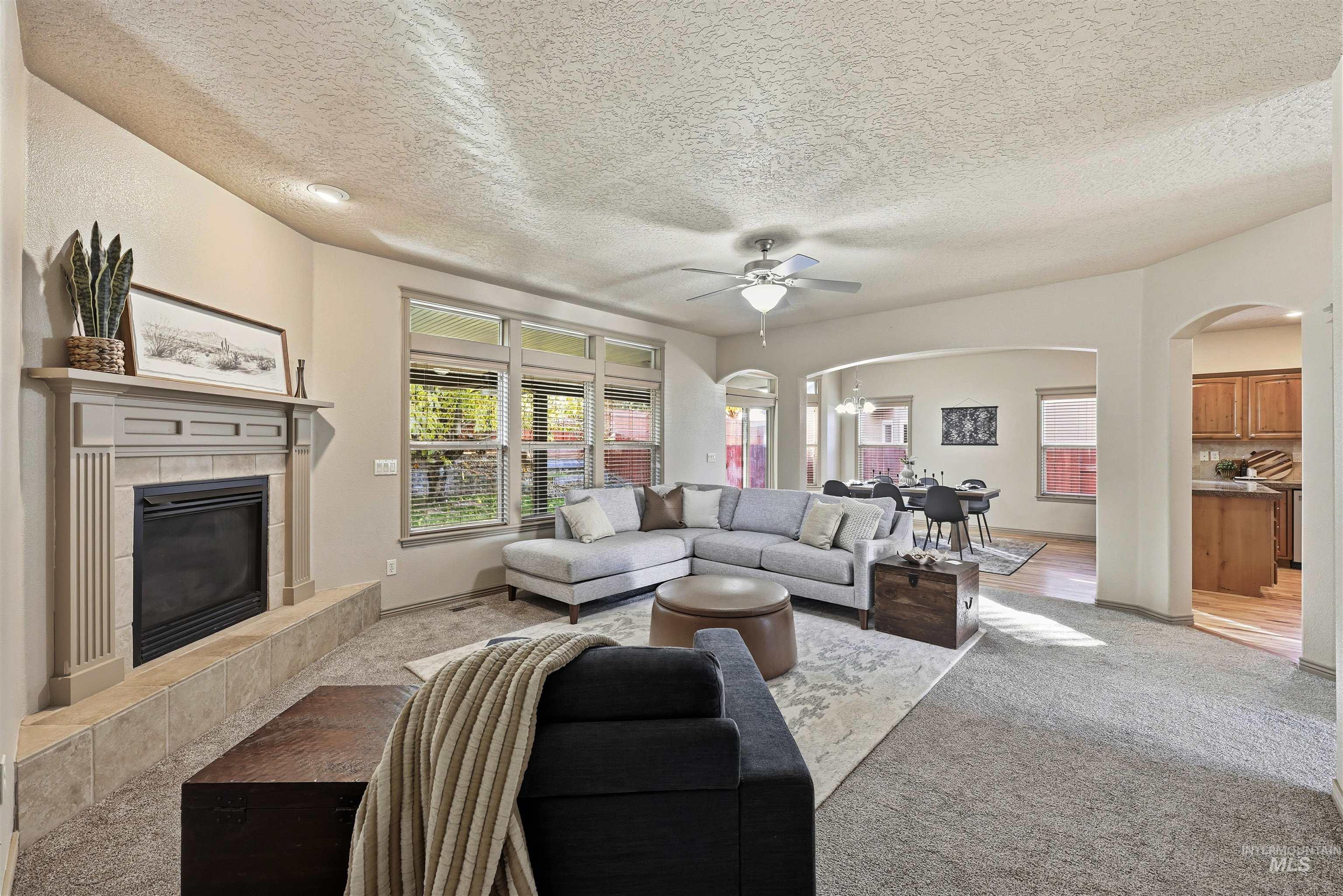 Living room featuring arched walkways, a fireplace, carpet, a ceiling fan, and a textured ceiling