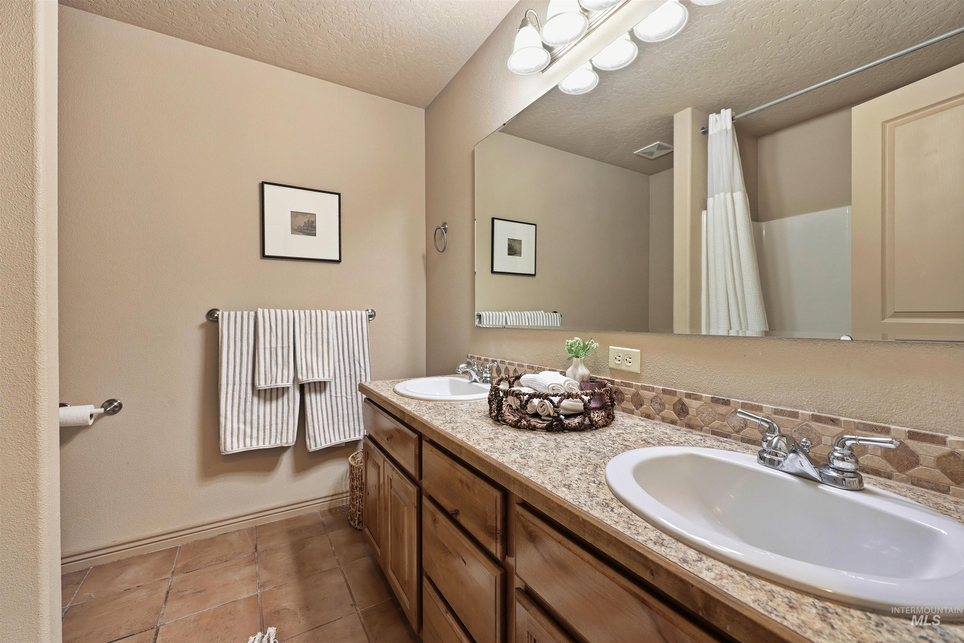 Full bathroom with a textured ceiling, double vanity, light tile patterned floors, and a shower with curtain