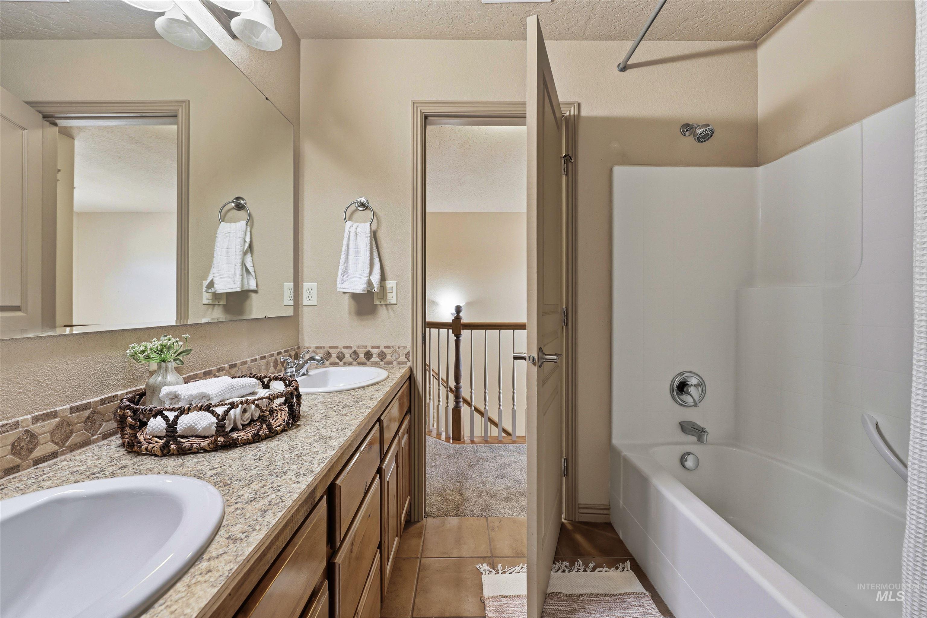 Bathroom featuring a textured ceiling, light tile patterned flooring, double vanity, and shower / bath combination with curtain