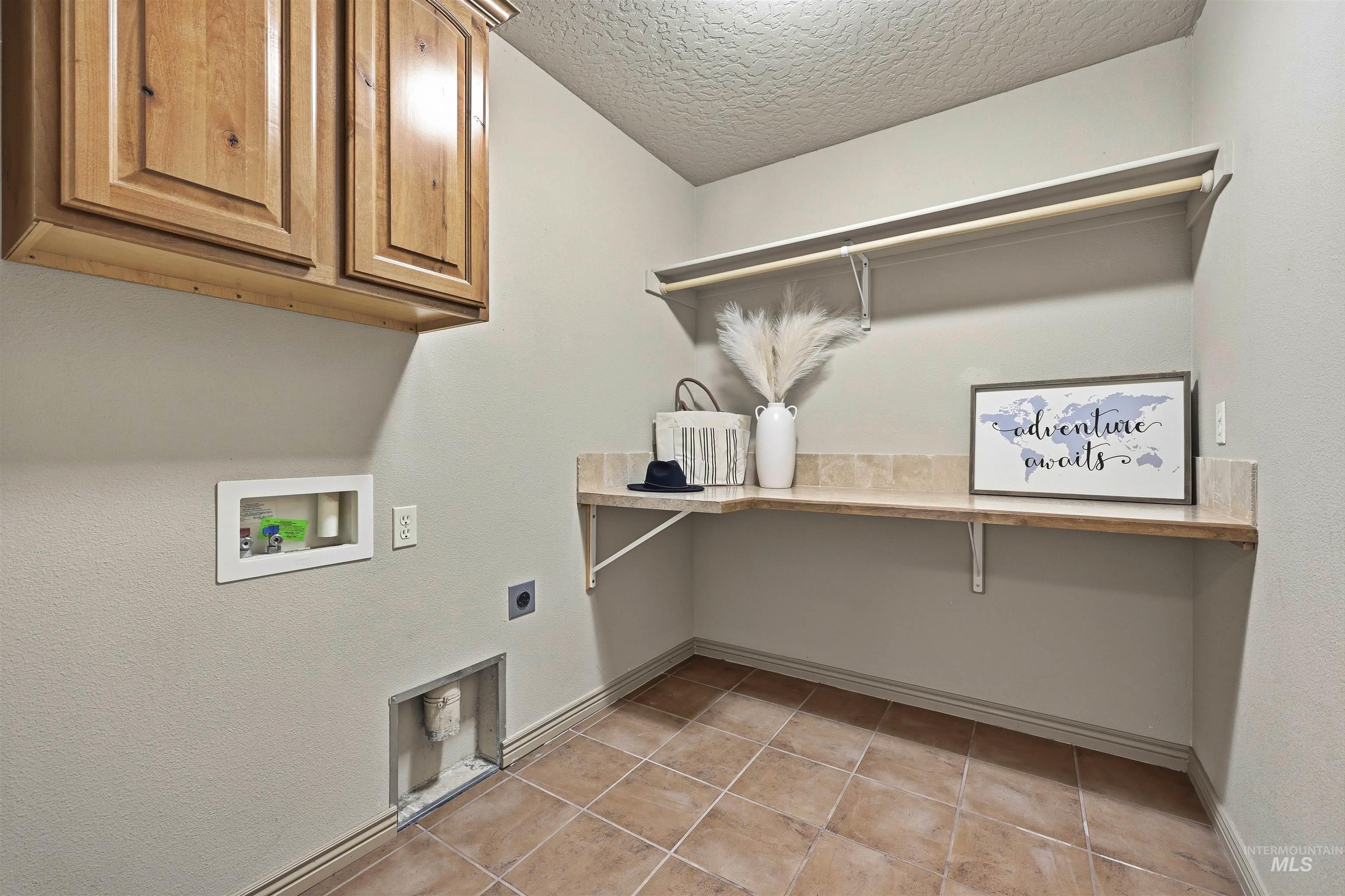 Laundry area with cabinet space, a textured ceiling, electric dryer hookup, hookup for a washing machine, and light tile patterned floors