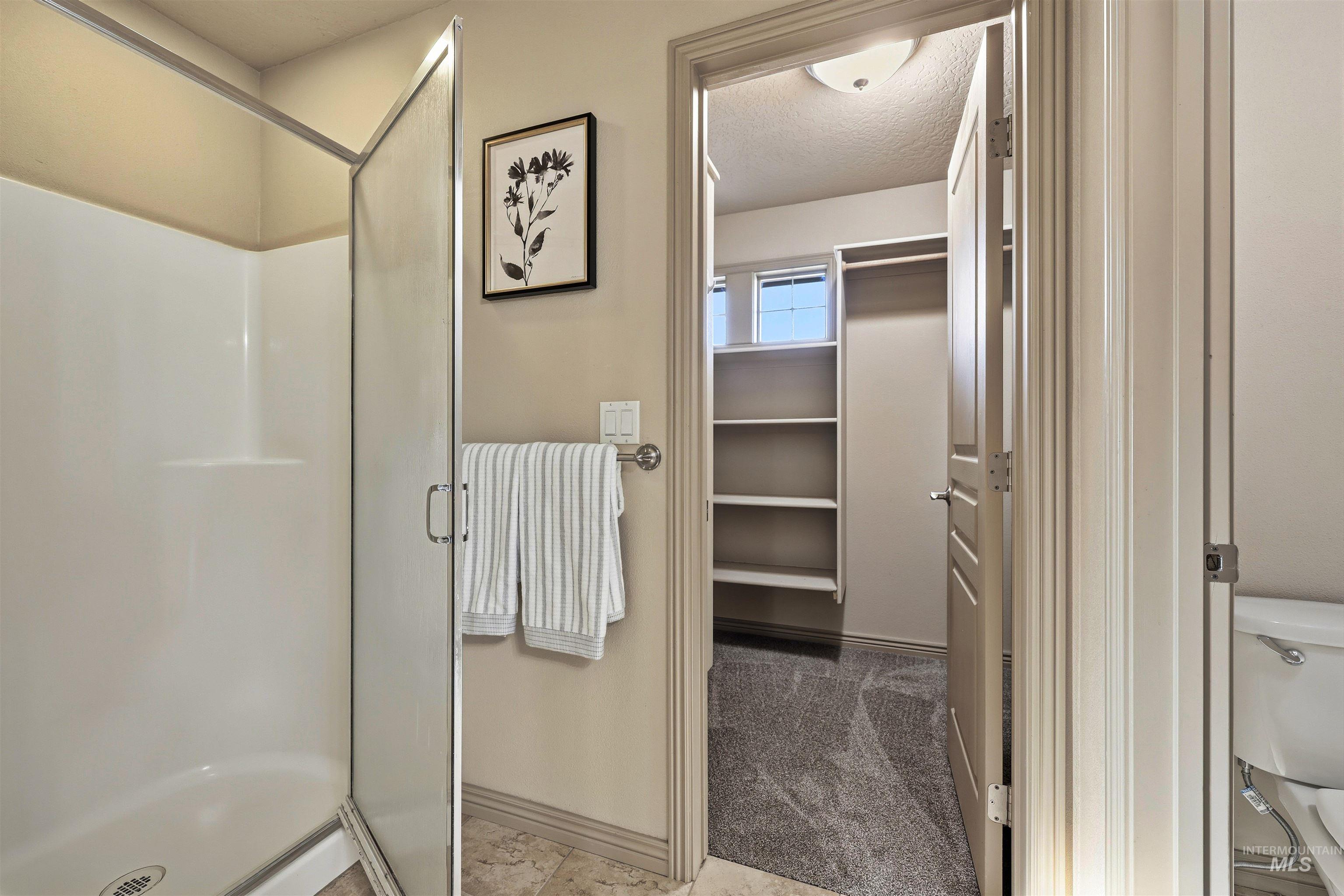 Full bathroom featuring a walk in closet, a shower stall, a textured ceiling, and light carpet