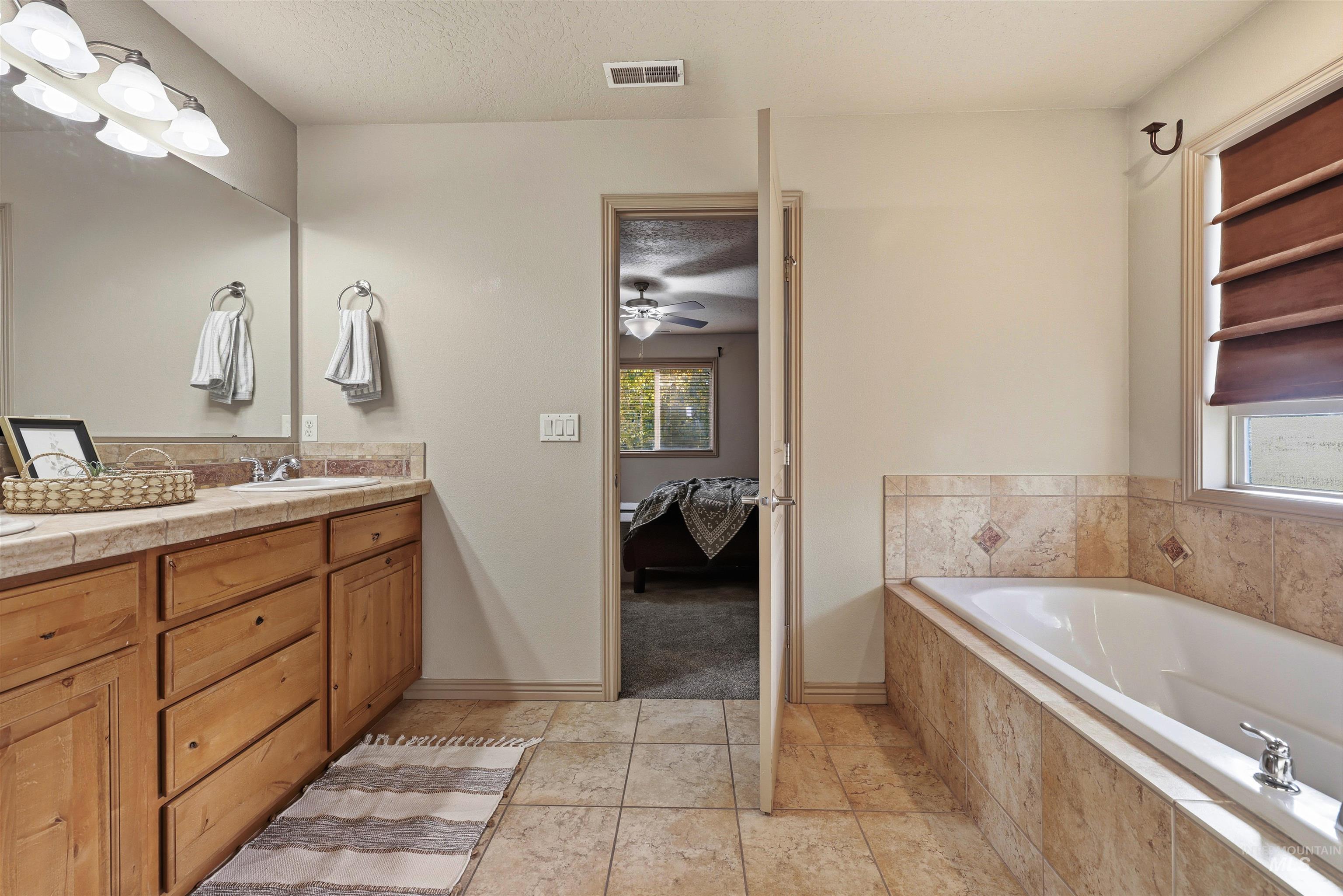 Full bathroom with connected bathroom, double vanity, a bath, a textured ceiling, and light tile patterned flooring