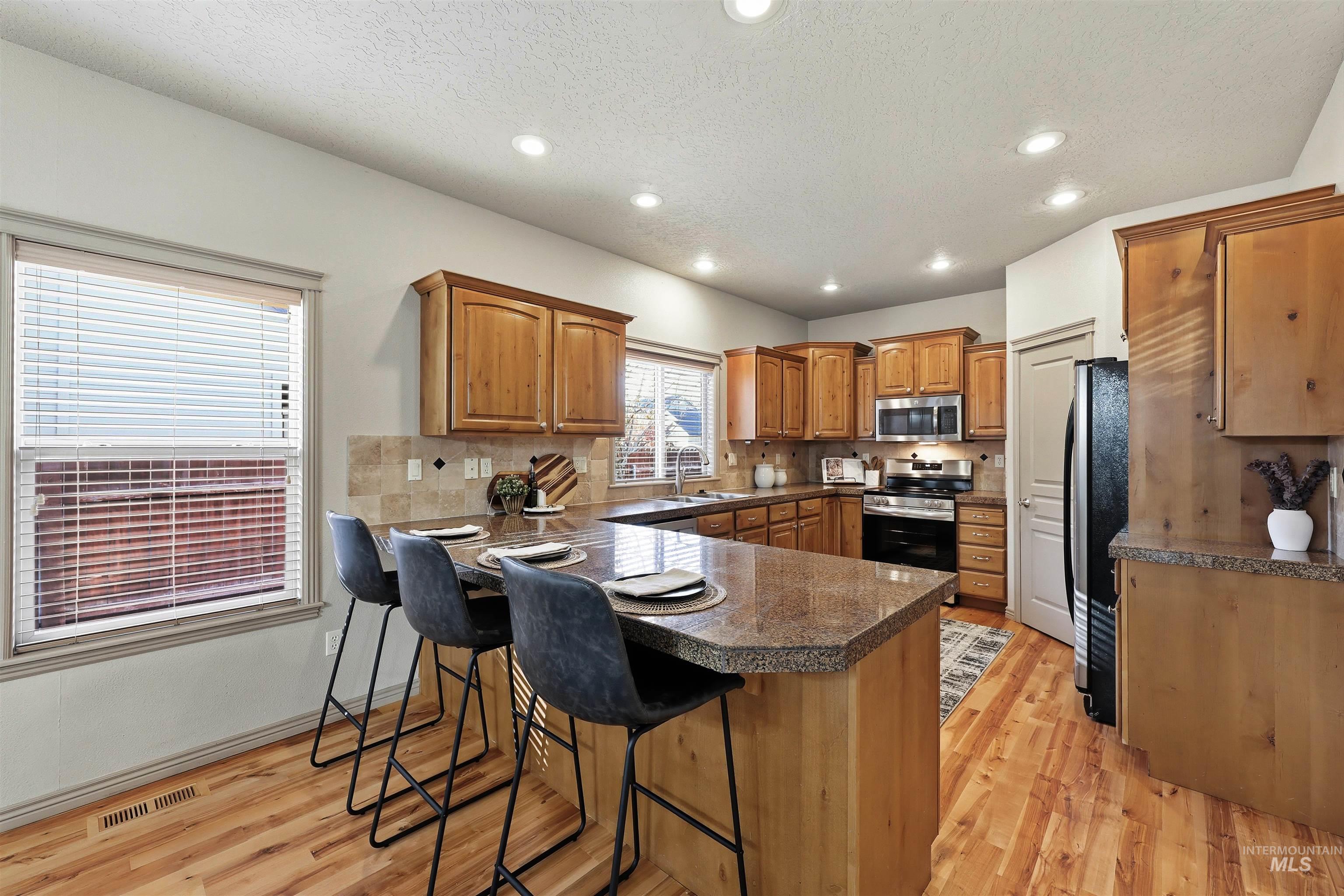 Kitchen with brown cabinets, light wood finished floors, recessed lighting, appliances with stainless steel finishes, and a kitchen breakfast bar