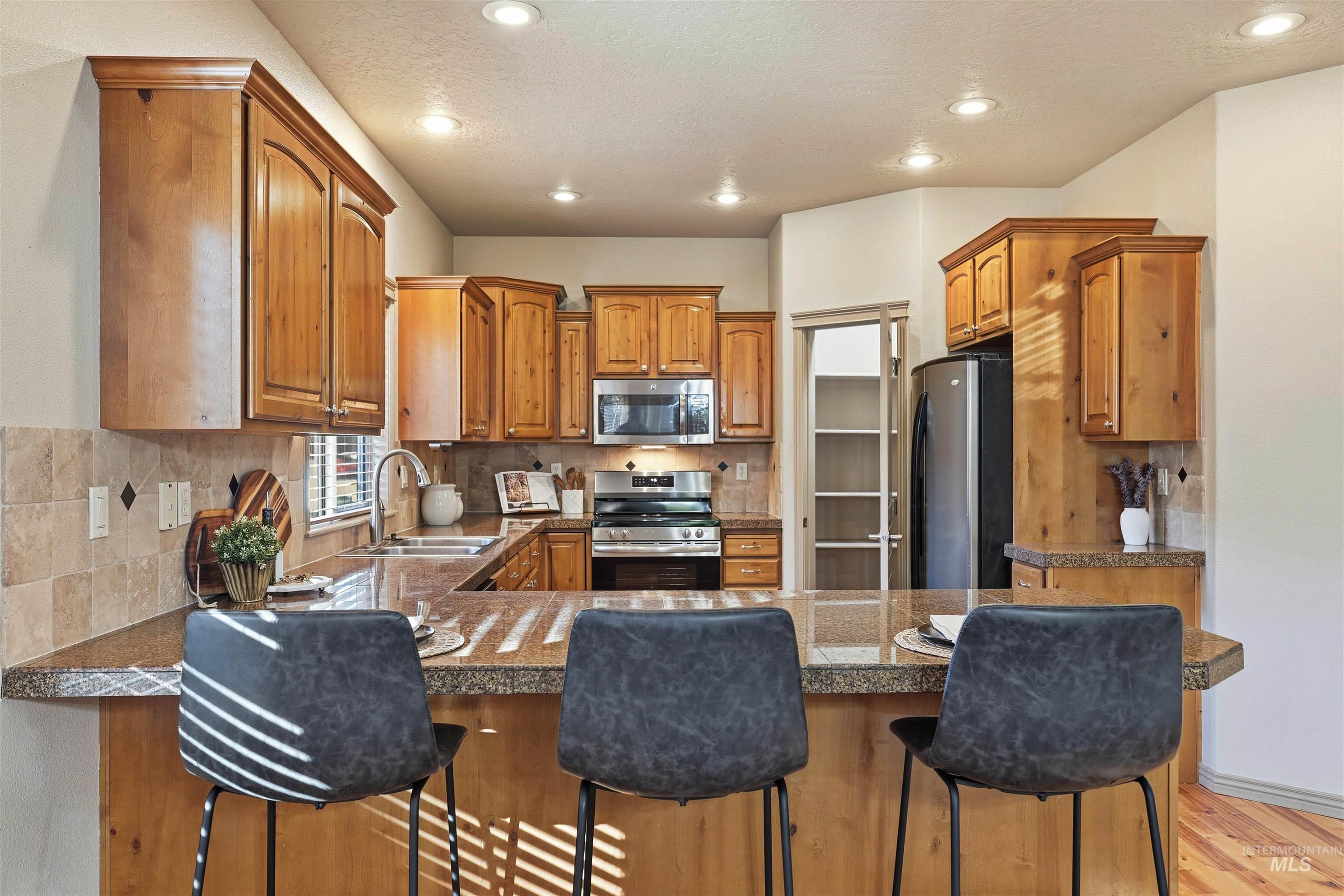 Kitchen featuring tasteful backsplash, brown cabinetry, stainless steel appliances, recessed lighting, and a breakfast bar area