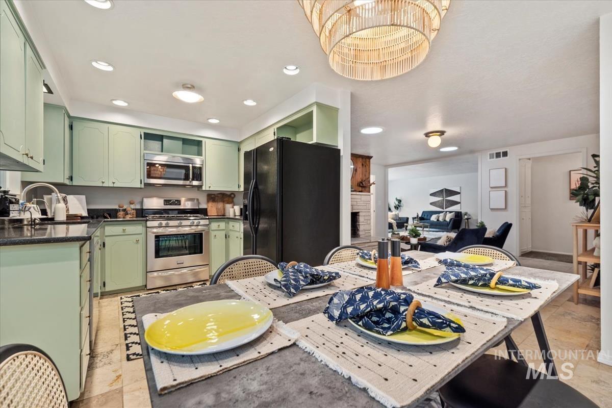 Kitchen with green cabinetry, stainless steel appliances, dark stone counters, recessed lighting, and a large fireplace