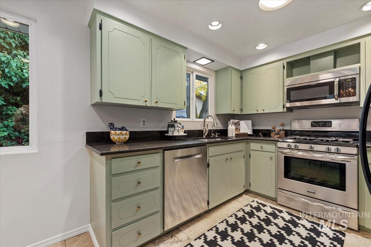 Kitchen featuring green cabinets, appliances with stainless steel finishes, recessed lighting, dark stone counters, and light tile patterned flooring
