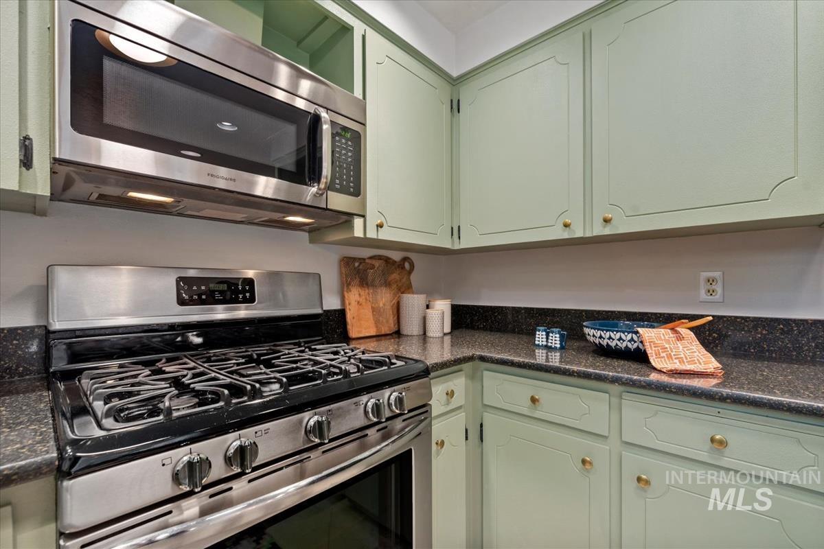 Kitchen with green cabinets, appliances with stainless steel finishes, and dark stone countertops