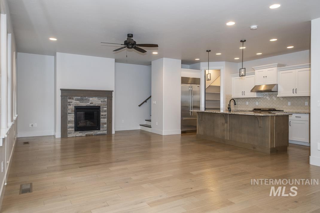 Kitchen with open floor plan, backsplash, white cabinets, hanging light fixtures, and light stone counters