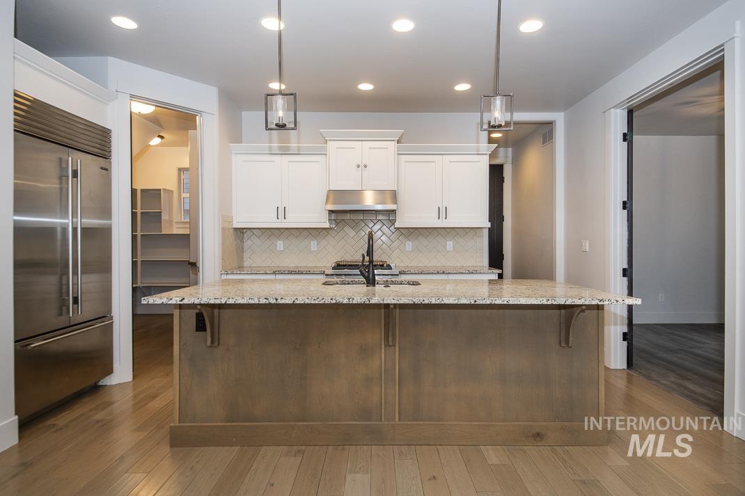 Kitchen with stainless steel built in refrigerator, backsplash, white cabinetry, dark wood finished floors, and decorative light fixtures