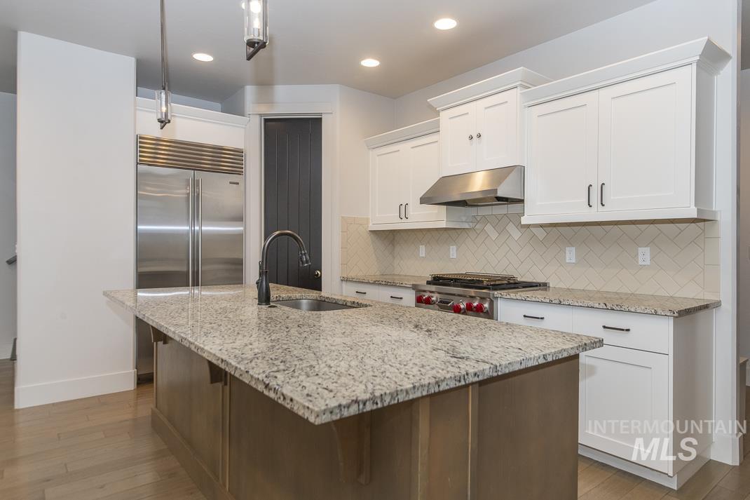 Kitchen featuring light stone counters, hanging light fixtures, tasteful backsplash, an island with sink, and light wood-style flooring