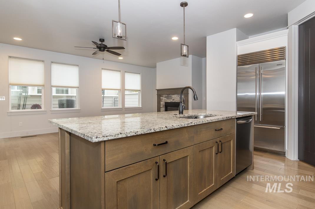 Kitchen featuring a center island with sink, appliances with stainless steel finishes, ceiling fan, decorative light fixtures, and light stone counters