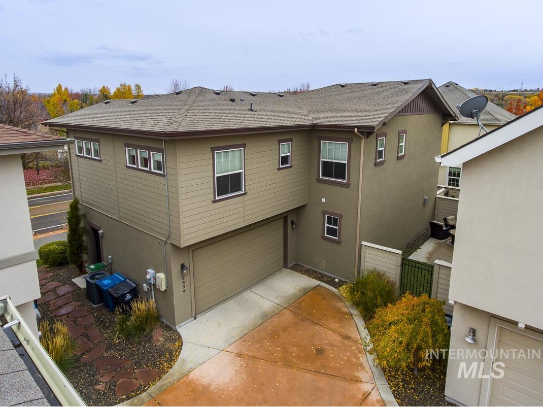 Rear view of property with stucco siding, a shingled roof, concrete driveway, and an attached garage