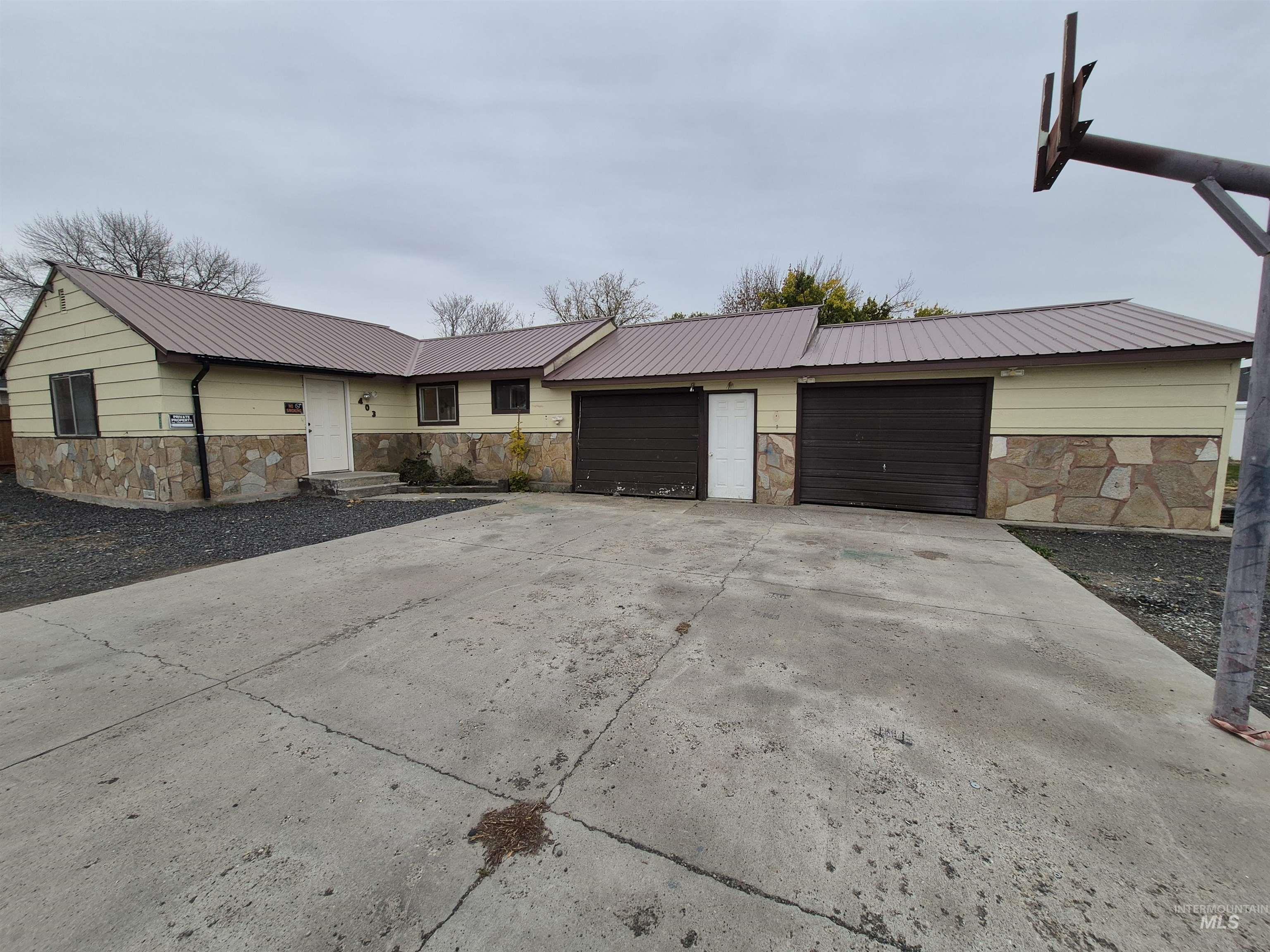 Ranch-style home with stone siding, a metal roof, a garage, and driveway