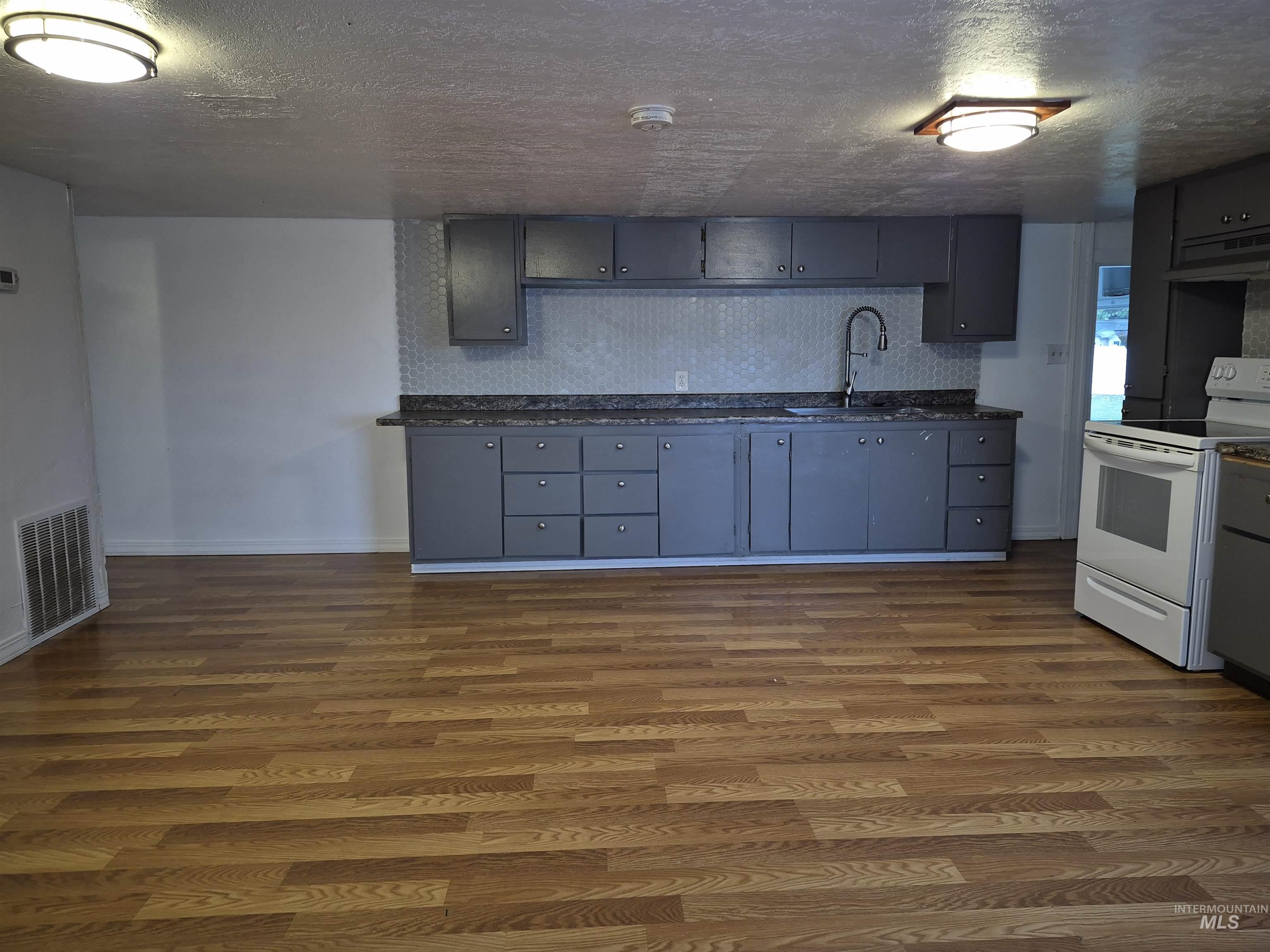 Kitchen with a textured ceiling, electric range, dark wood-type flooring, gray cabinetry, and ventilation hood