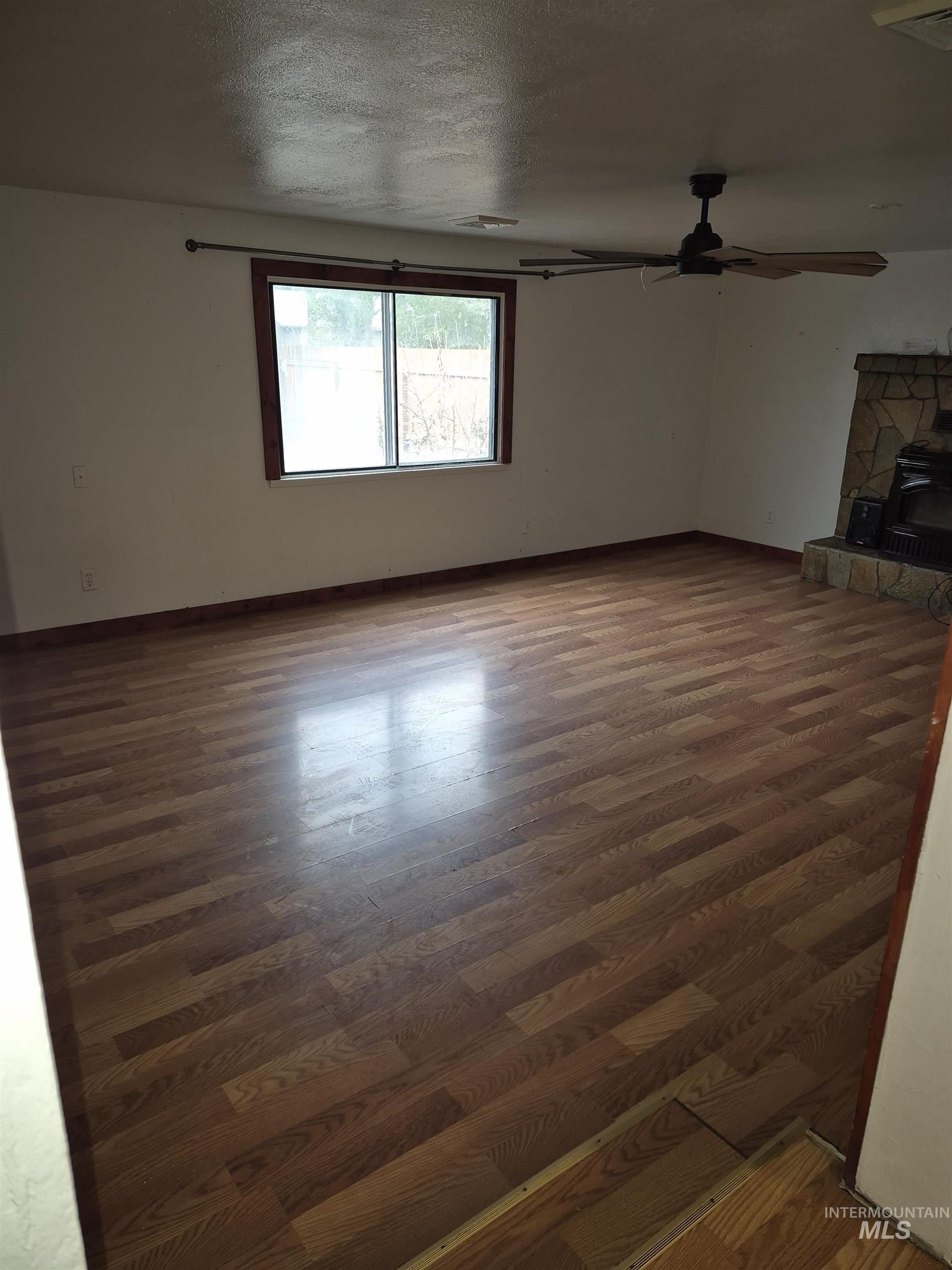 Unfurnished living room with a wood stove, dark wood finished floors, a textured ceiling, and ceiling fan