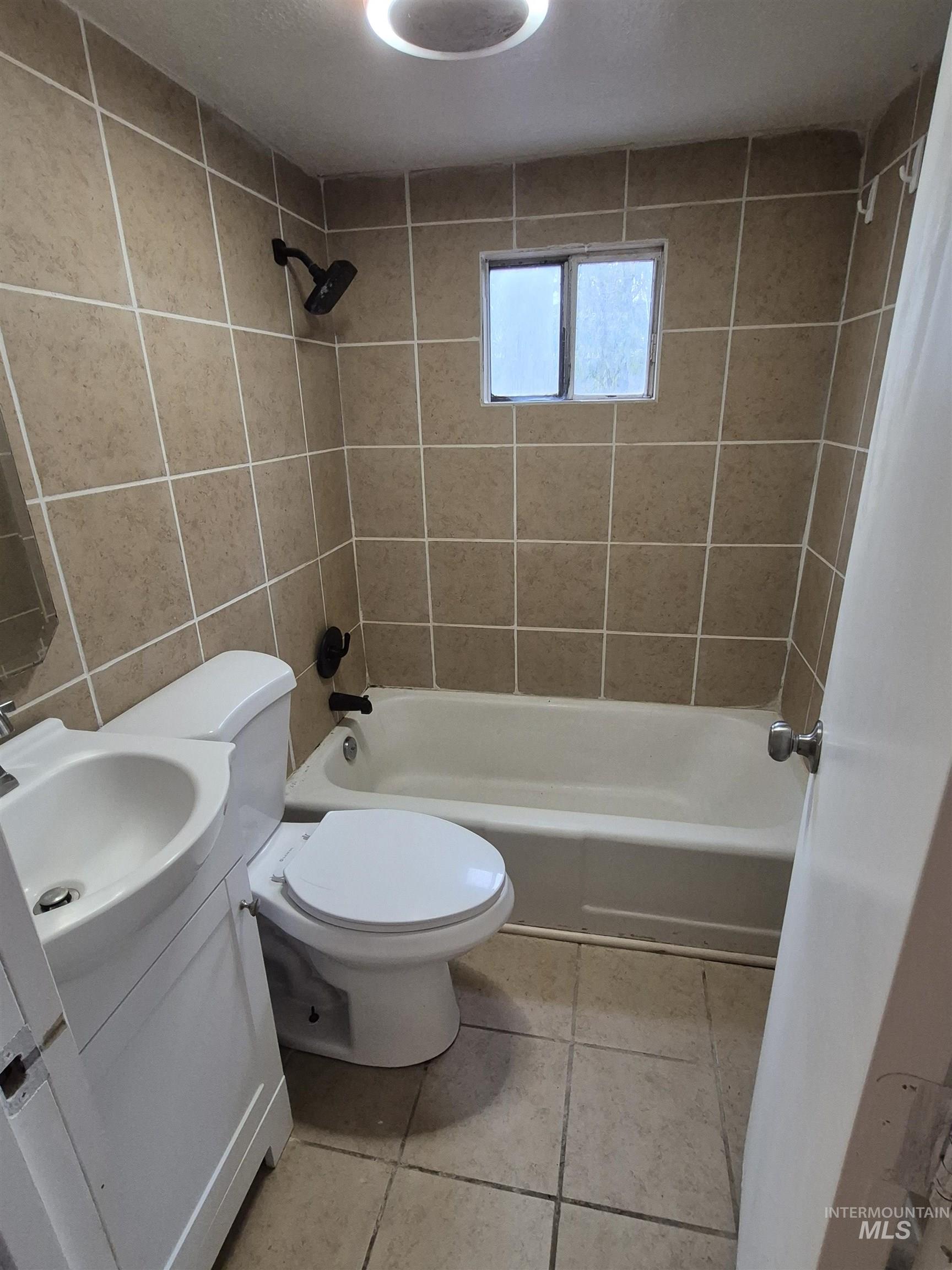 Full bath featuring vanity, light tile patterned floors, shower / bathtub combination with curtain, and tile walls