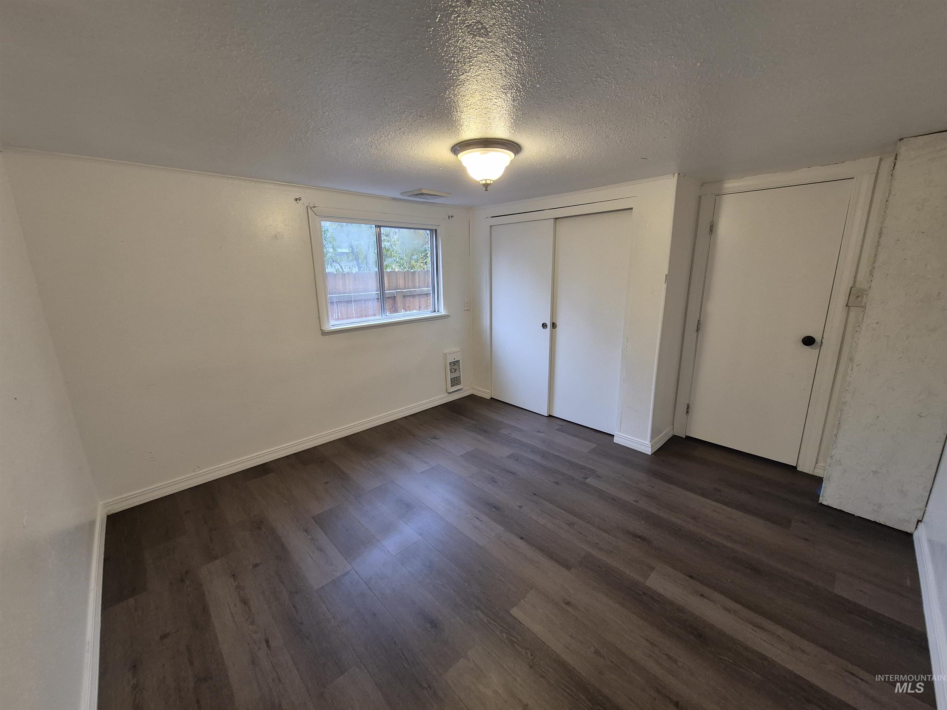 Unfurnished bedroom with a textured ceiling, dark wood-type flooring, a closet, and heating unit