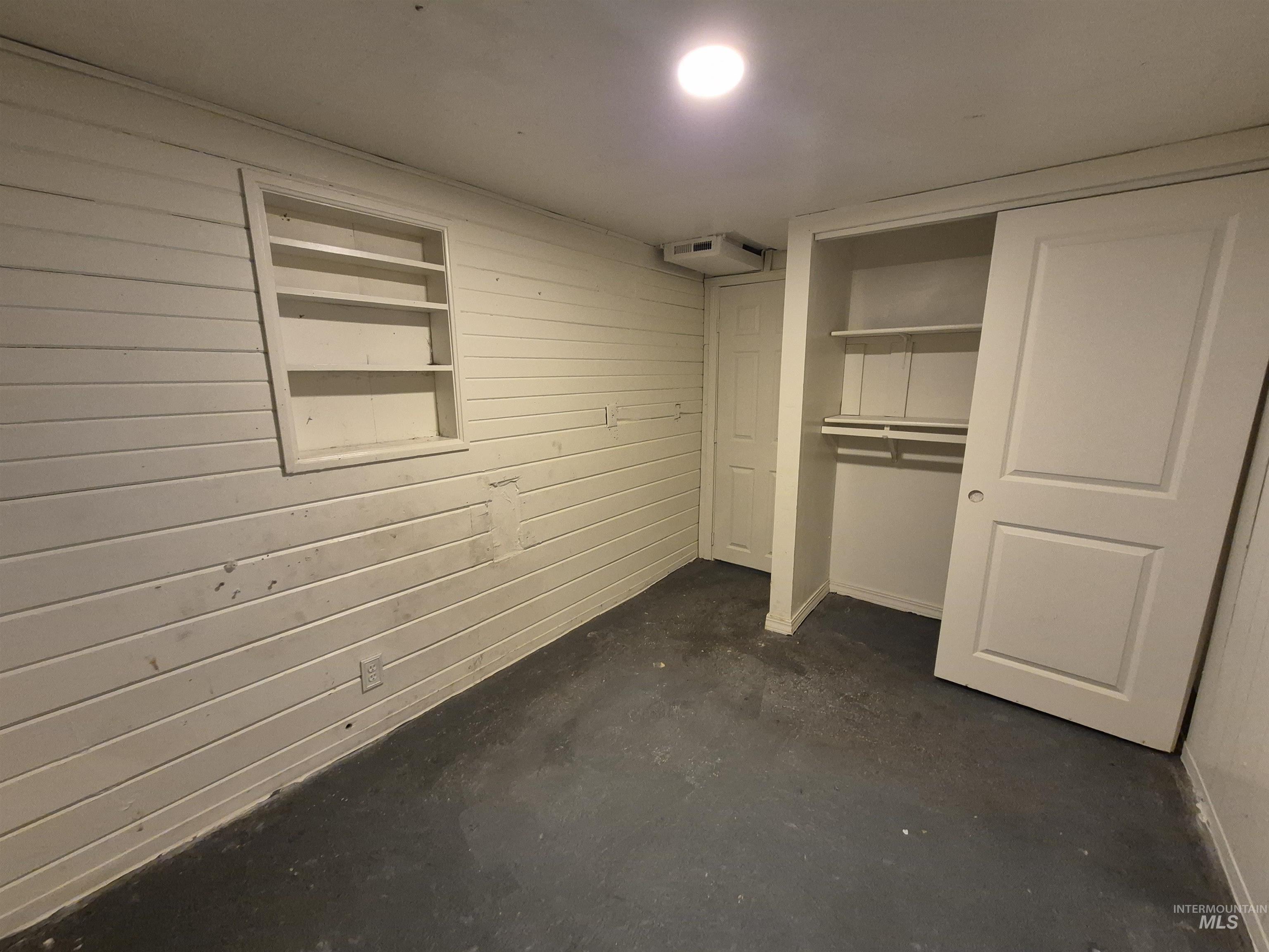 Unfurnished bedroom featuring wood walls, concrete flooring, and a closet