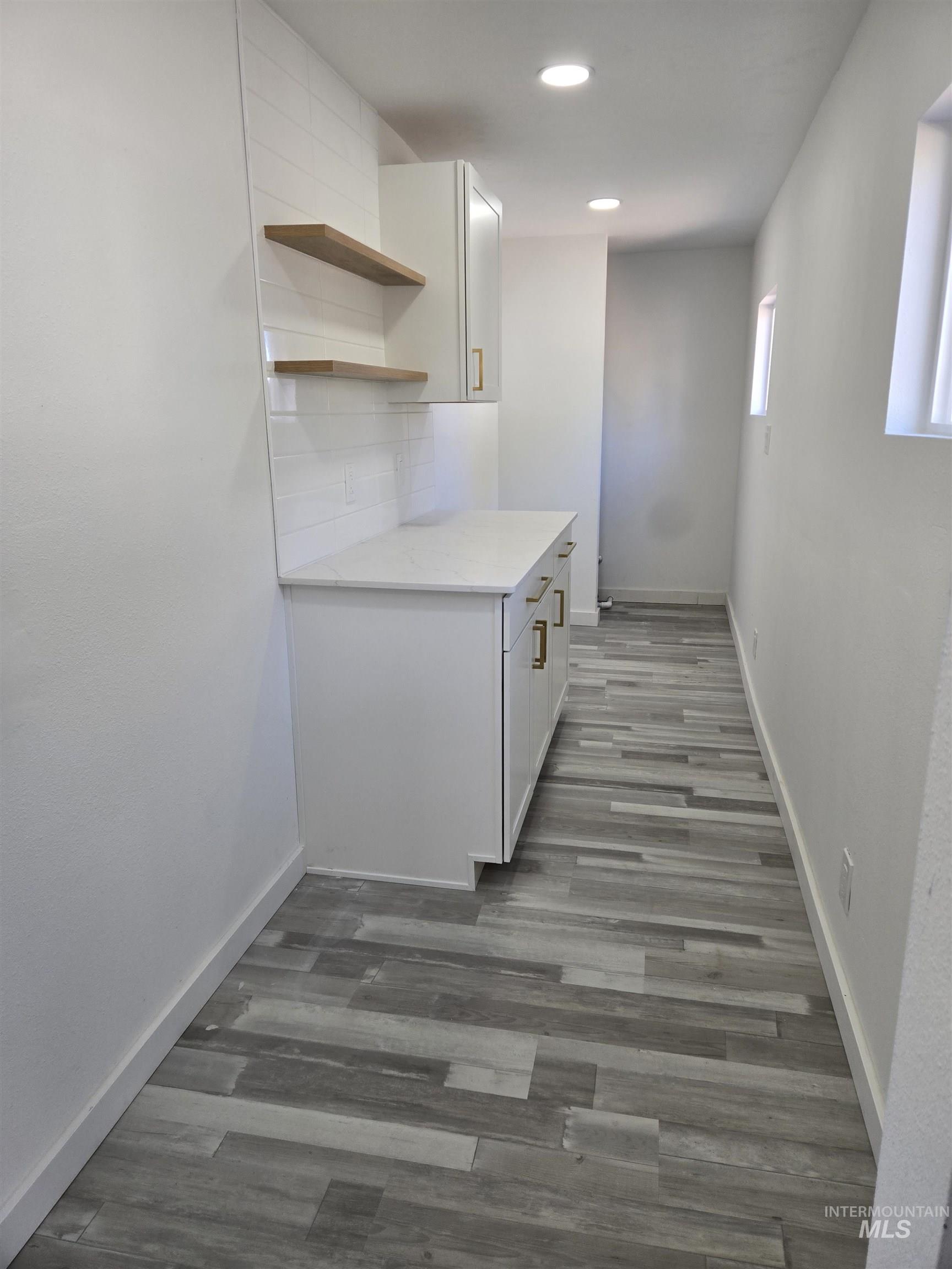 Kitchen featuring white cabinetry, light wood-style flooring, open shelves, tasteful backsplash, and light stone countertops