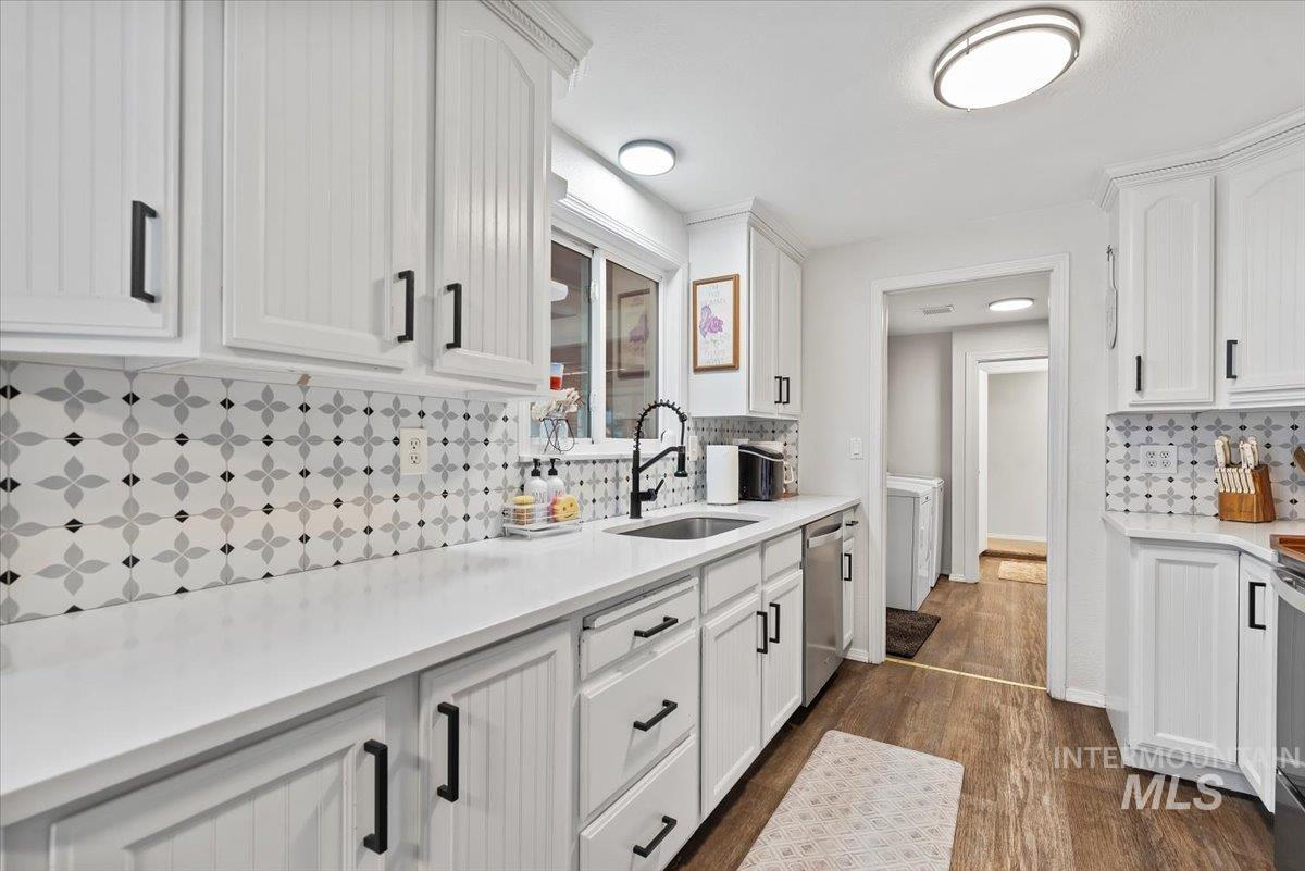 Kitchen with tasteful backsplash, dark wood-style floors, white cabinetry, and light stone countertops