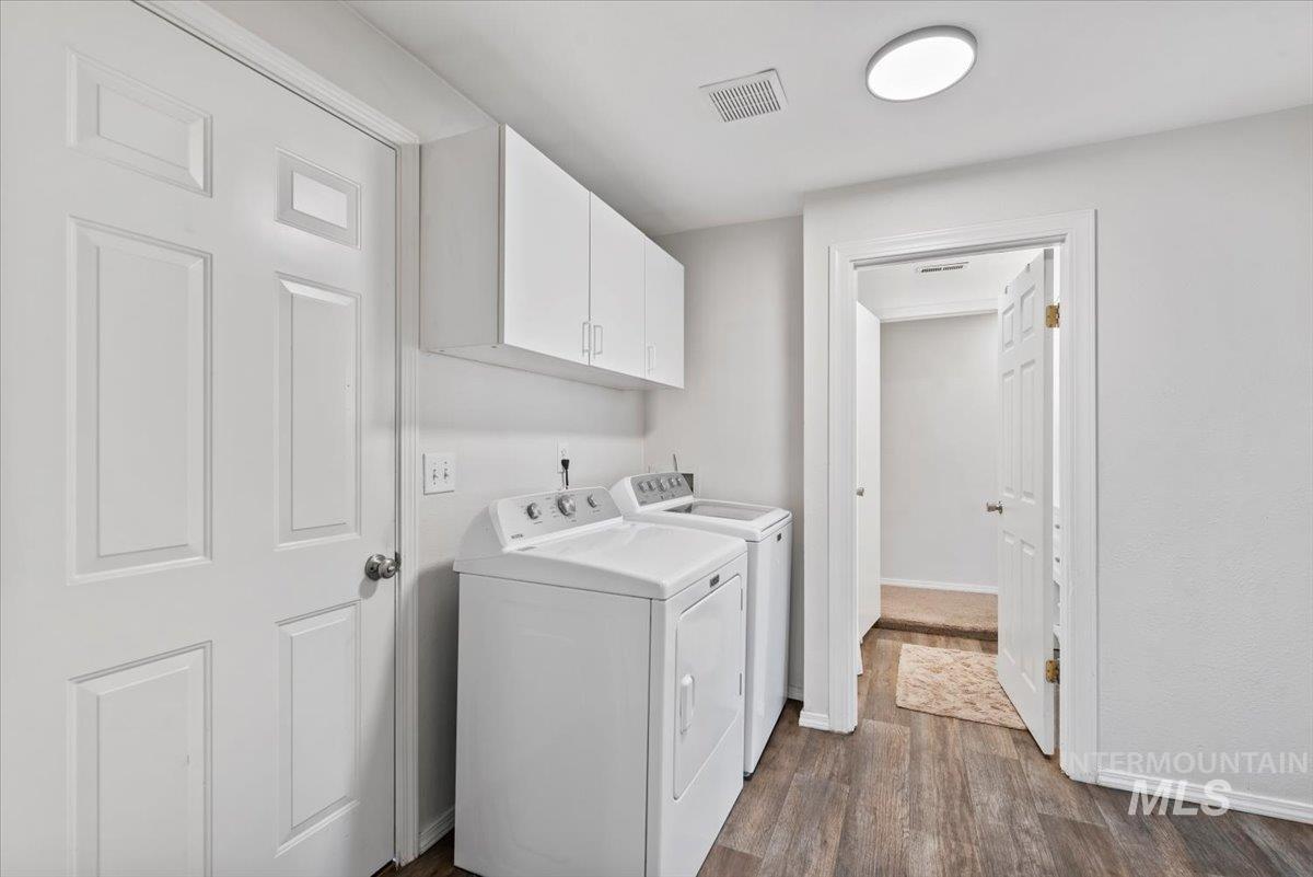 Washroom featuring dark wood finished floors, washer and dryer, and cabinet space