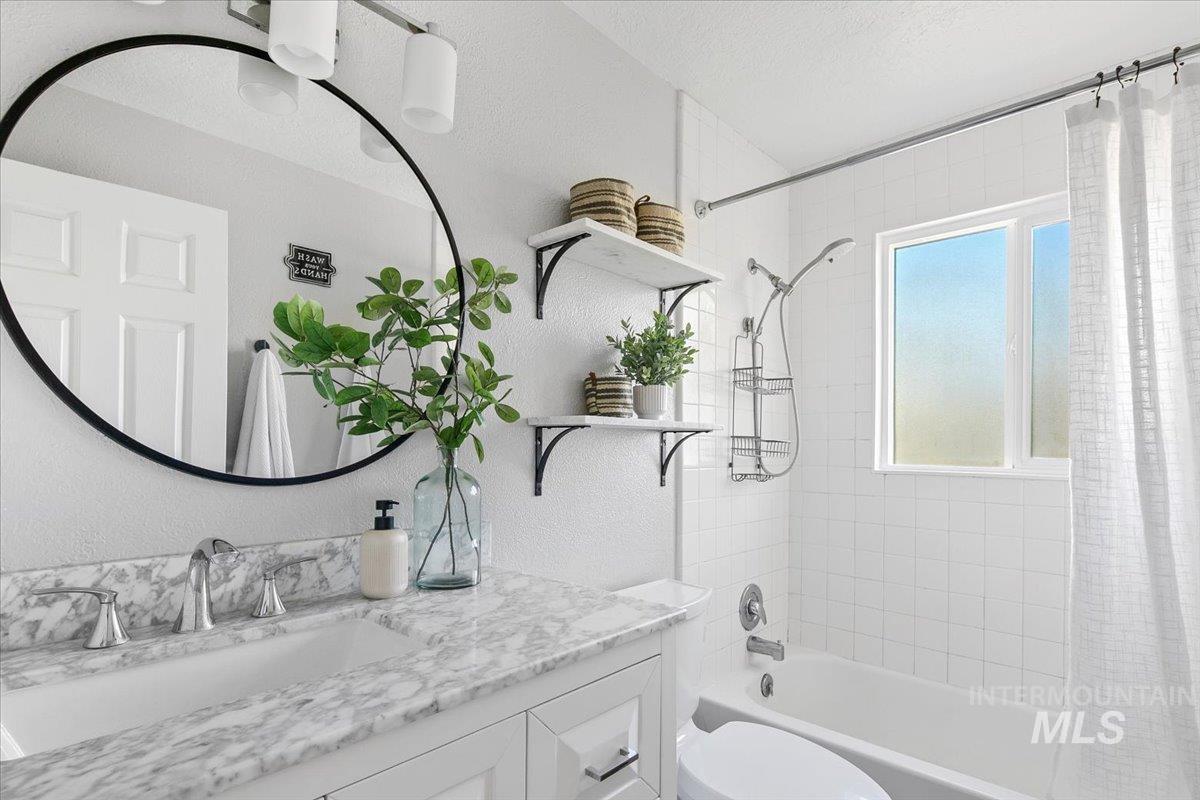 Bathroom featuring shower / tub combo with curtain, a textured wall, and vanity